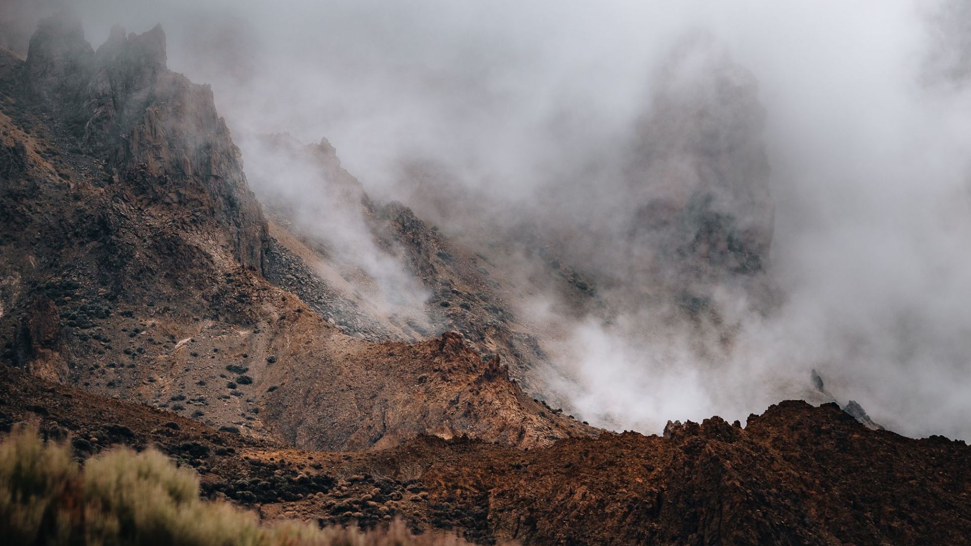 A dramatic landscape featuring rocky mountain sides shrouded in thick mist and fog.