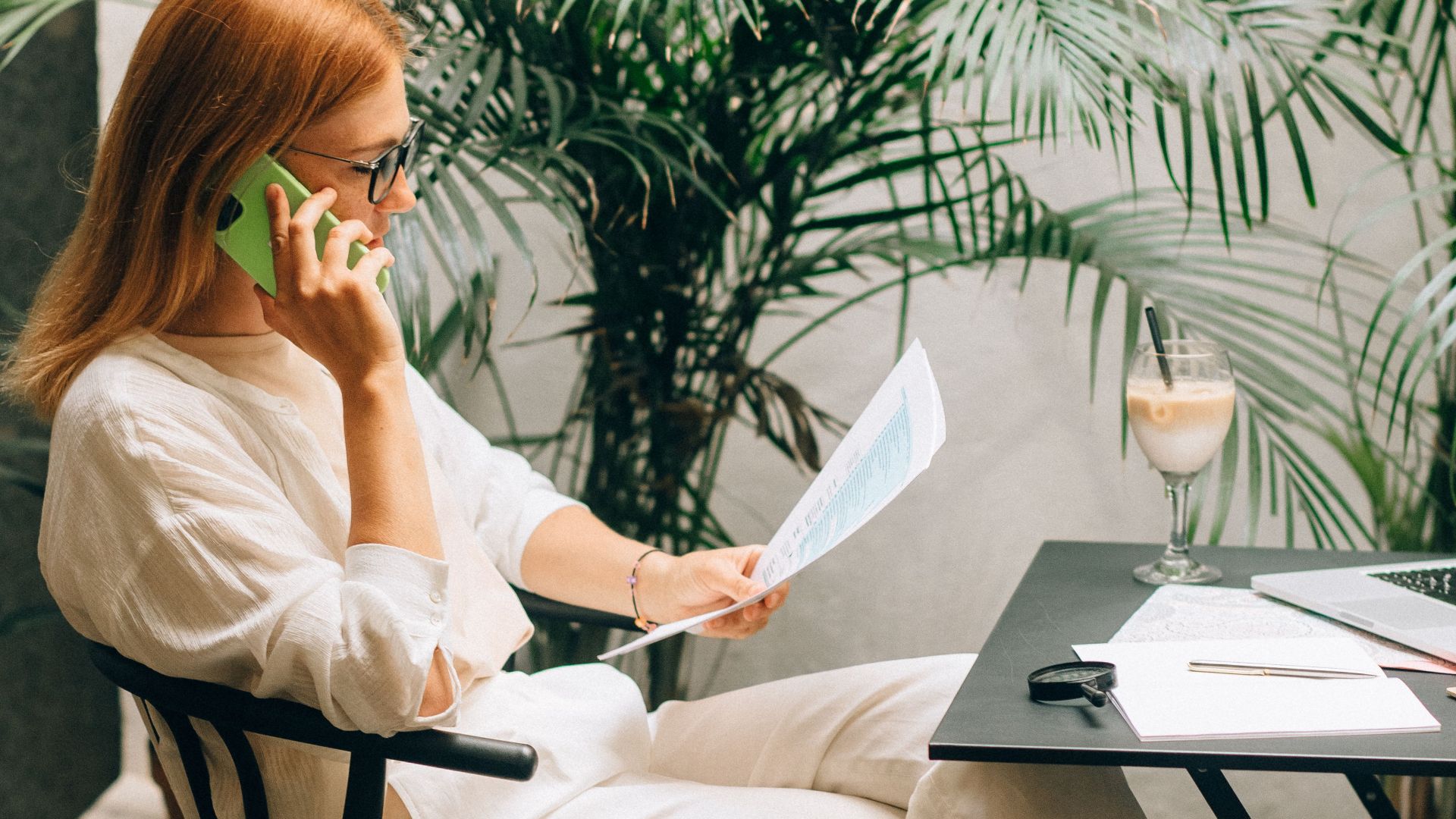 Professional woman working on documents and phone in a serene outdoor office setting.