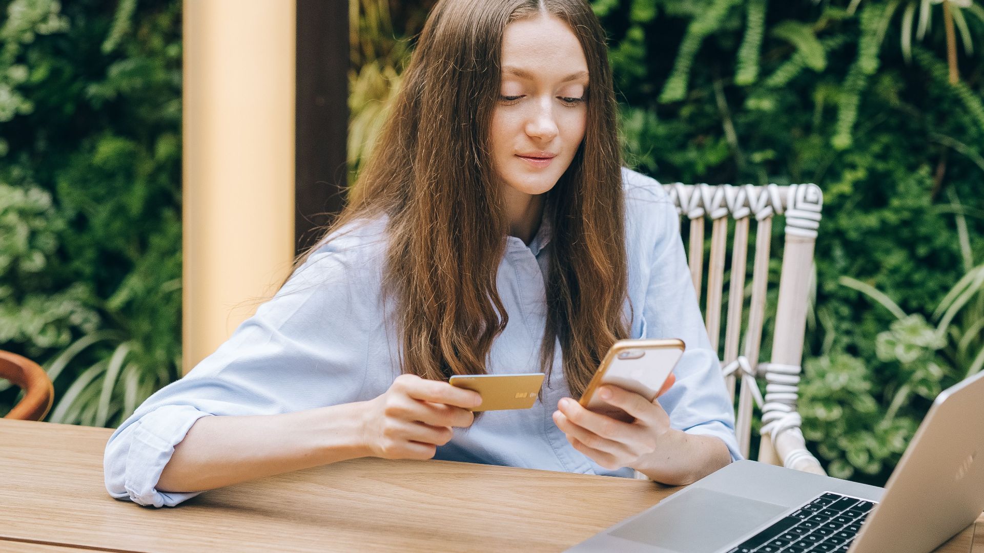 Young woman using smartphone and credit card for online shopping outdoors.