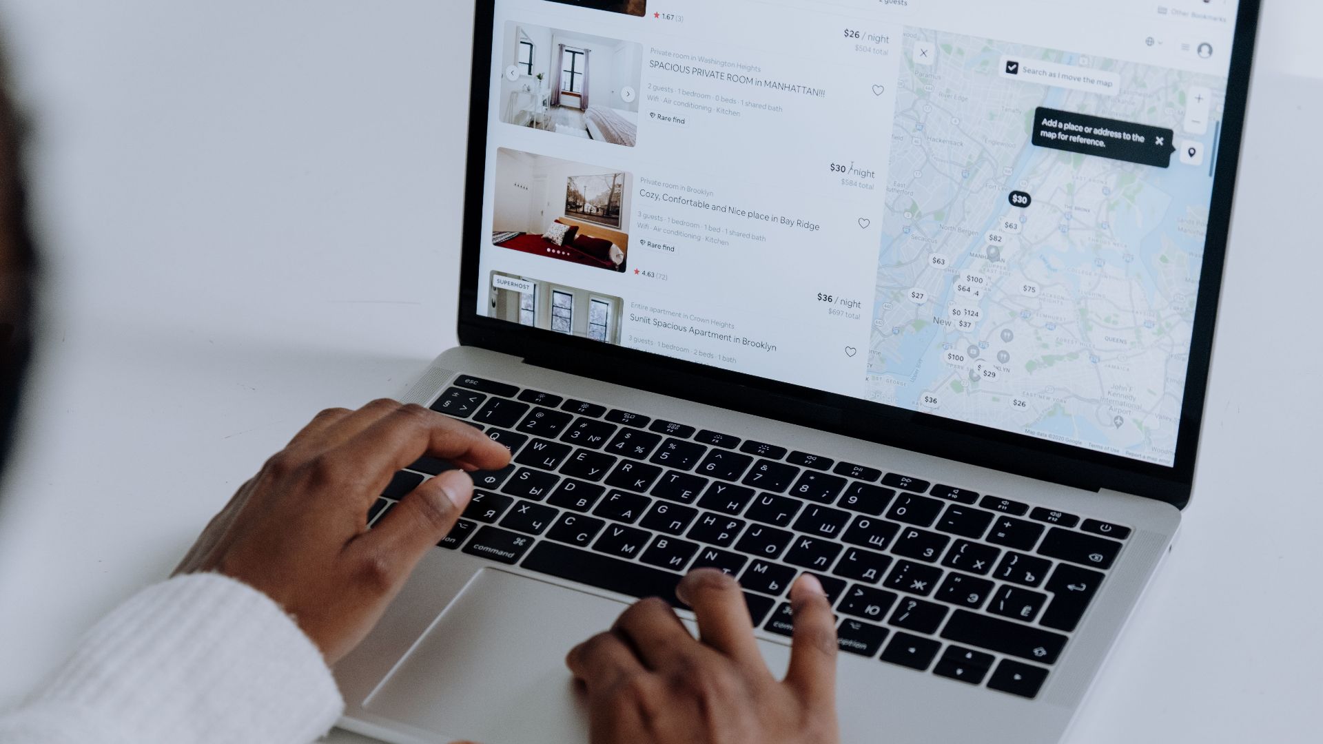Hands typing on laptop searching Airbnb for accommodation options with map view.