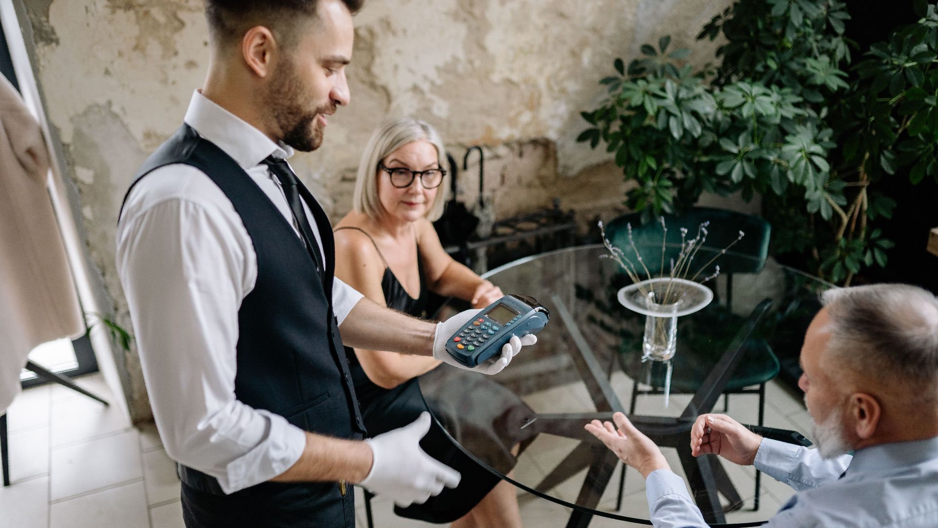 Senior couple completes payment with waiter in stylish restaurant setting, showcasing hospitality service.