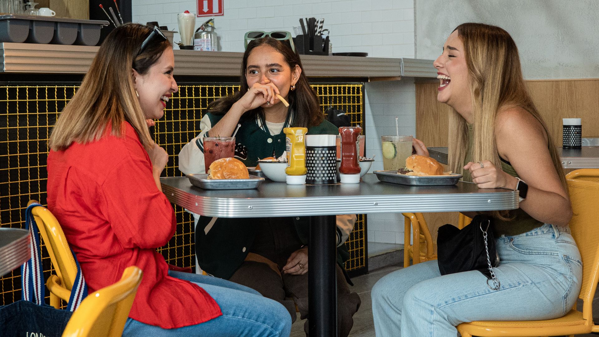 Three friends laughing and enjoying burgers in a vibrant city cafe.