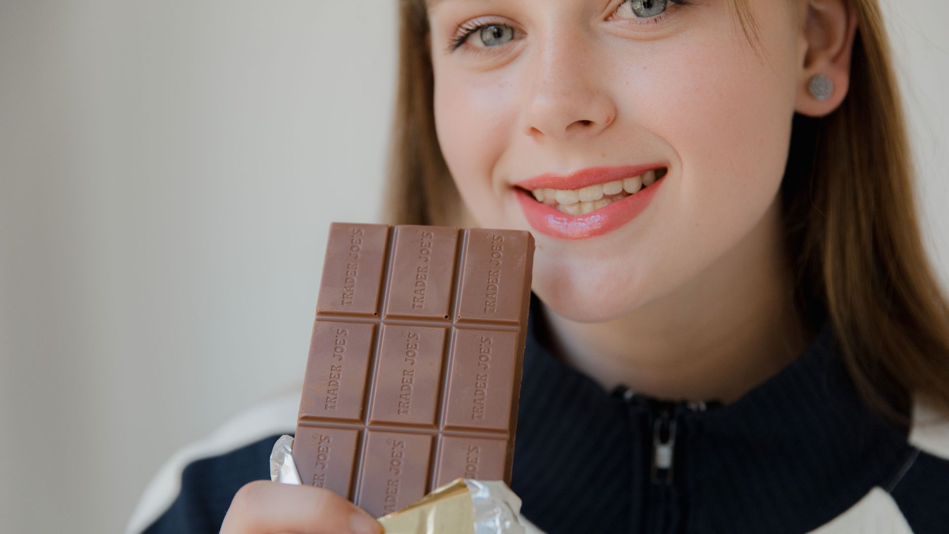 Smiling woman holding a chocolate bar, enjoying the sweet treat.