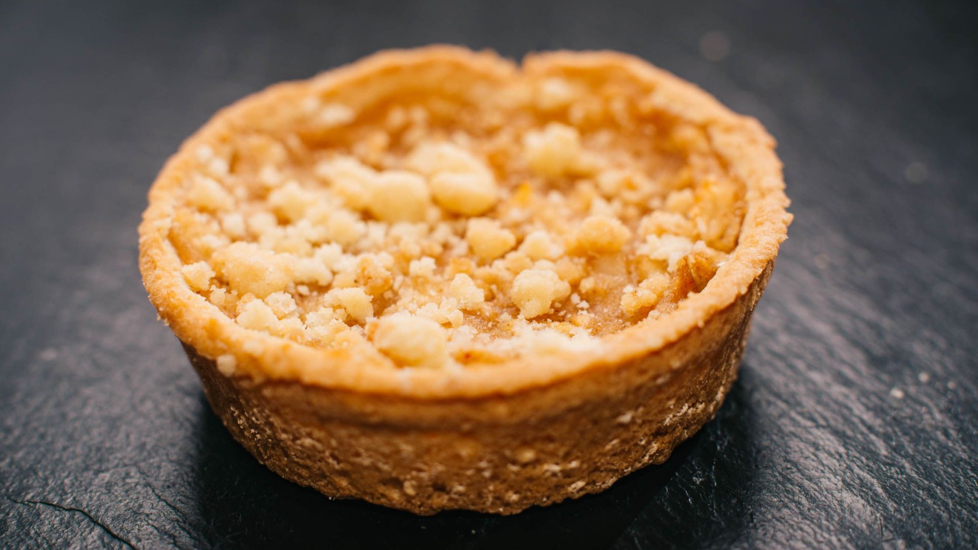 A mouth-watering apple crumble tart on a dark slate background.