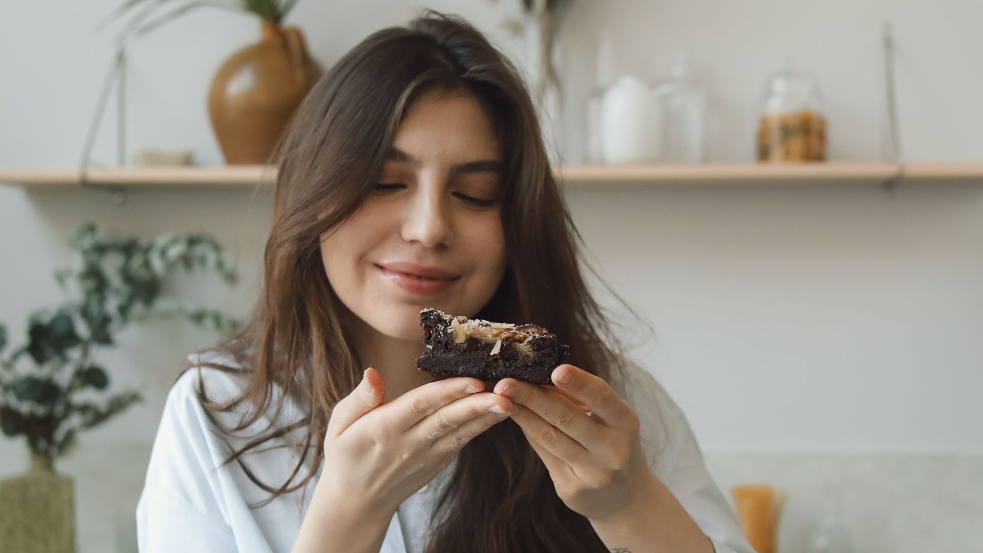 Smiling woman savoring a chocolate dessert indoors with natural light.