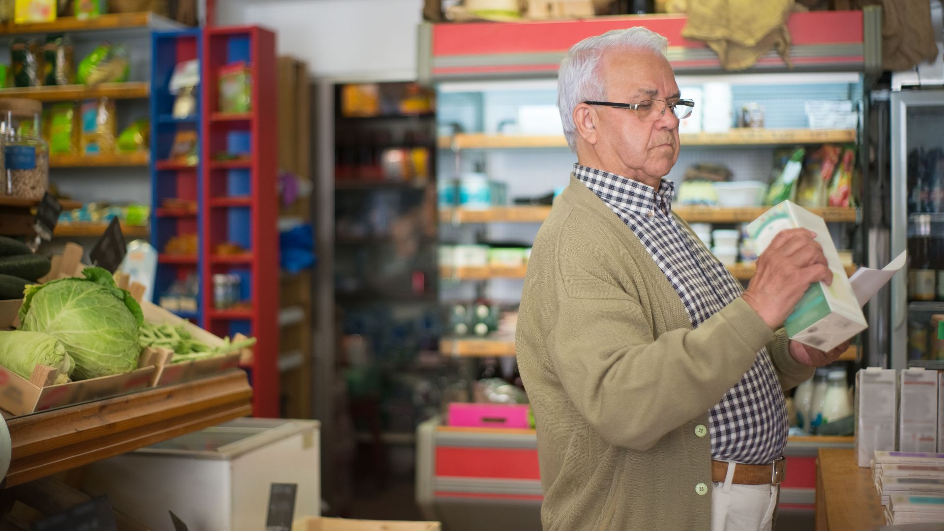 Senior man in a cardigan browsing products in a Portuguese grocery store.
