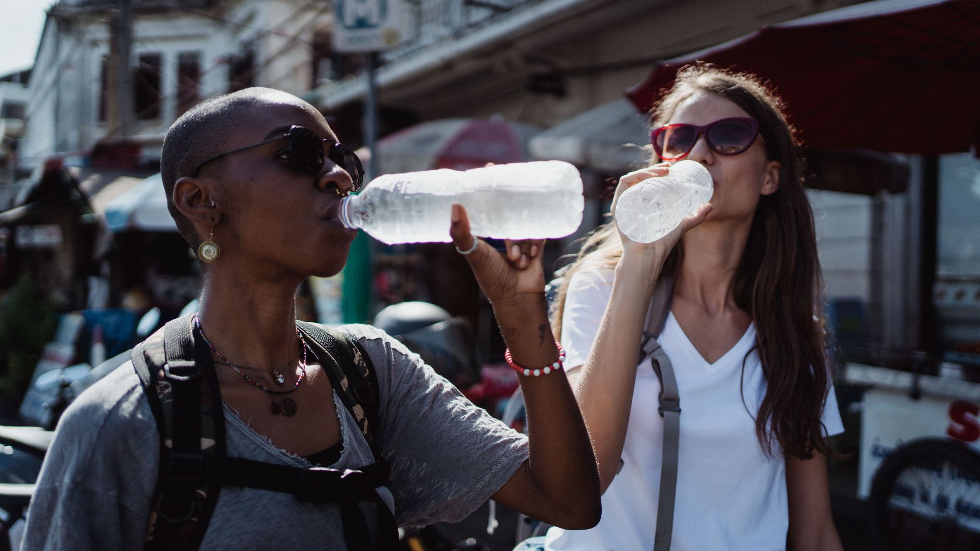Two women quenching their thirst with bottled water during a sunny outdoor adventure.