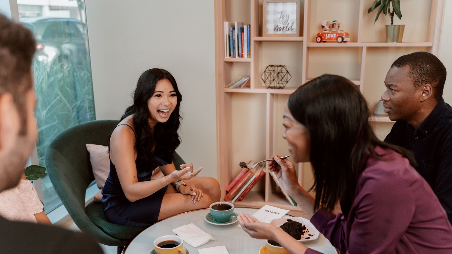 A diverse group of friends laughing and enjoying coffee and cake at a cozy café.