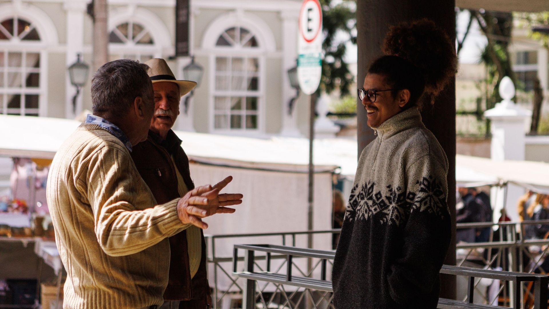 Three men casually chatting in an outdoor market in Curitiba, Brazil, captured during a sunny day.