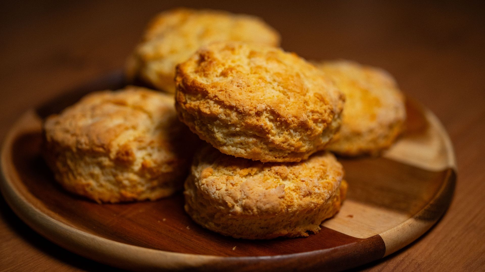 Freshly baked golden biscuits stacked on a wooden plate, perfect for breakfast or tea time.