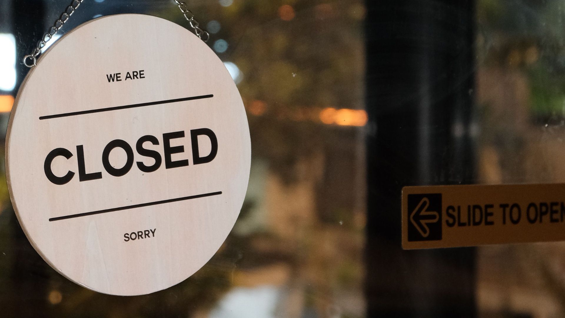 A glass door with a 'Closed' sign in a café at night, signifying closure.