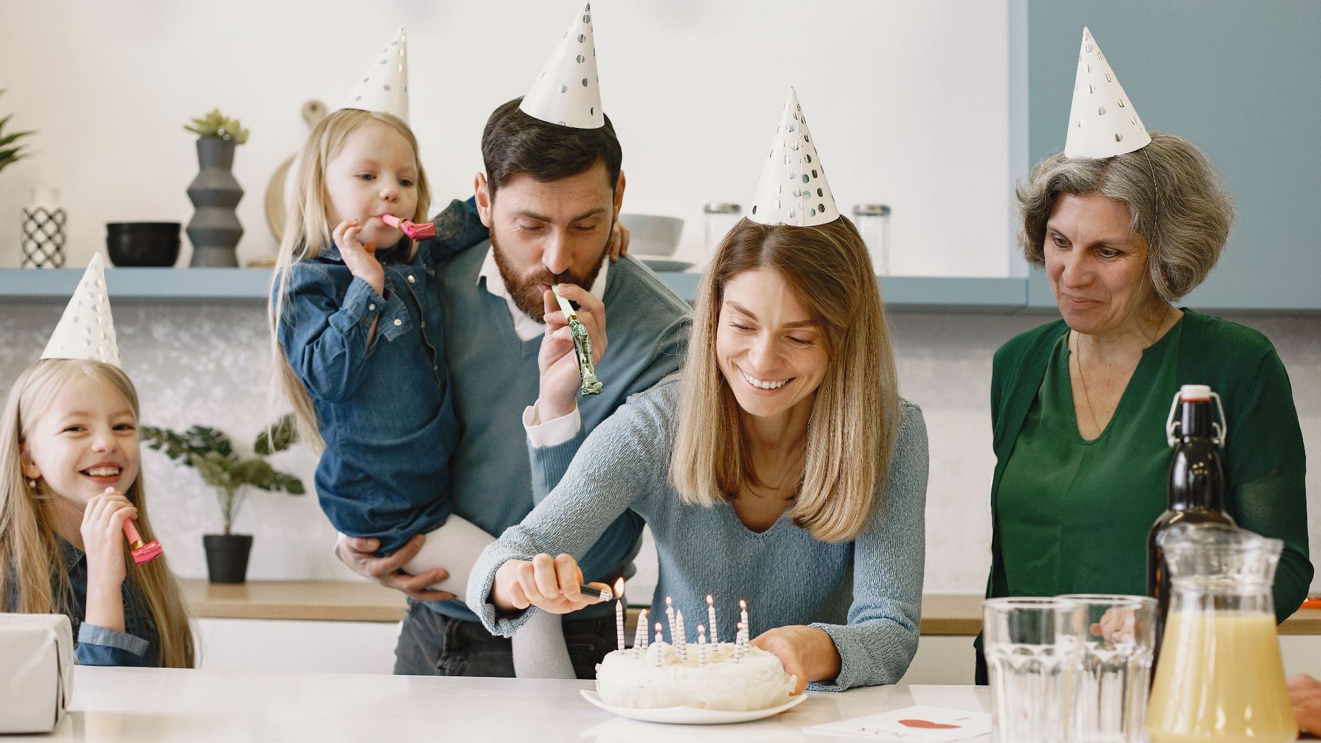 Joyful family gathering celebrating a birthday with a cake, candles, and party hats.