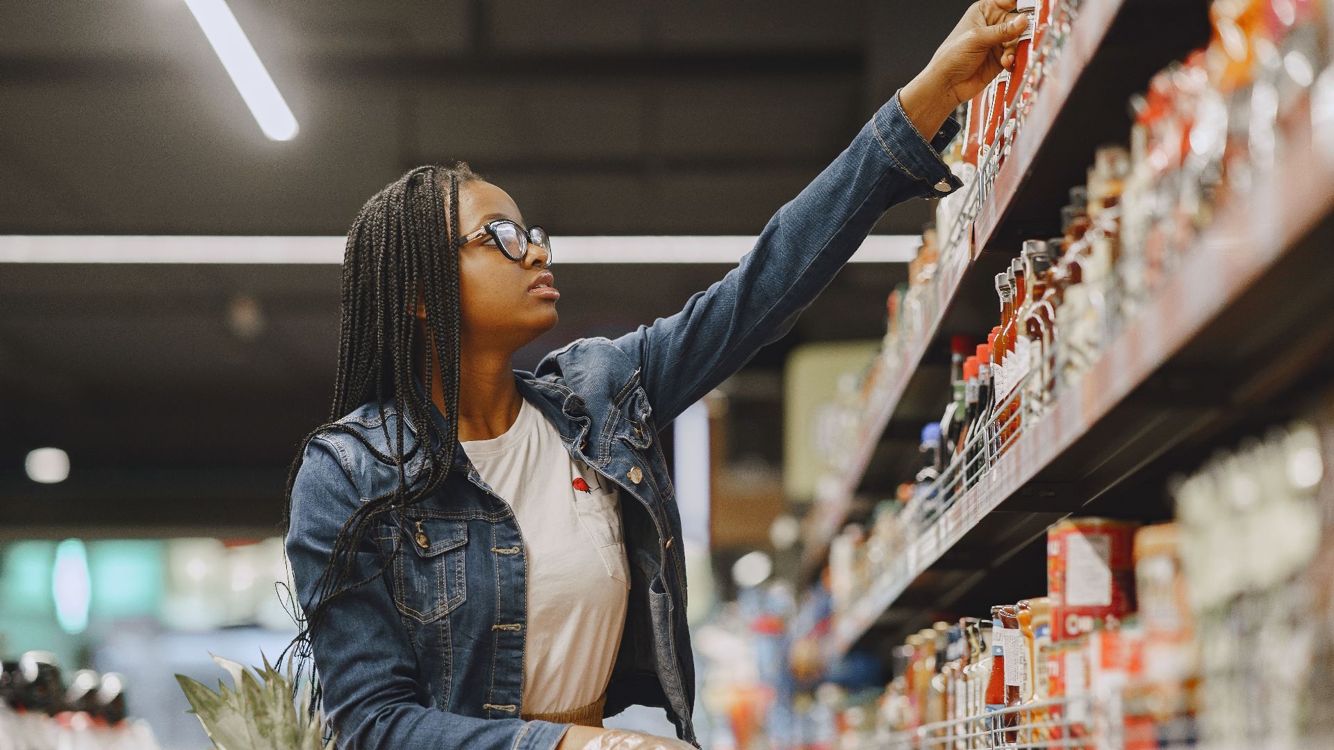 African American woman selecting items in a grocery store aisle with a shopping cart.