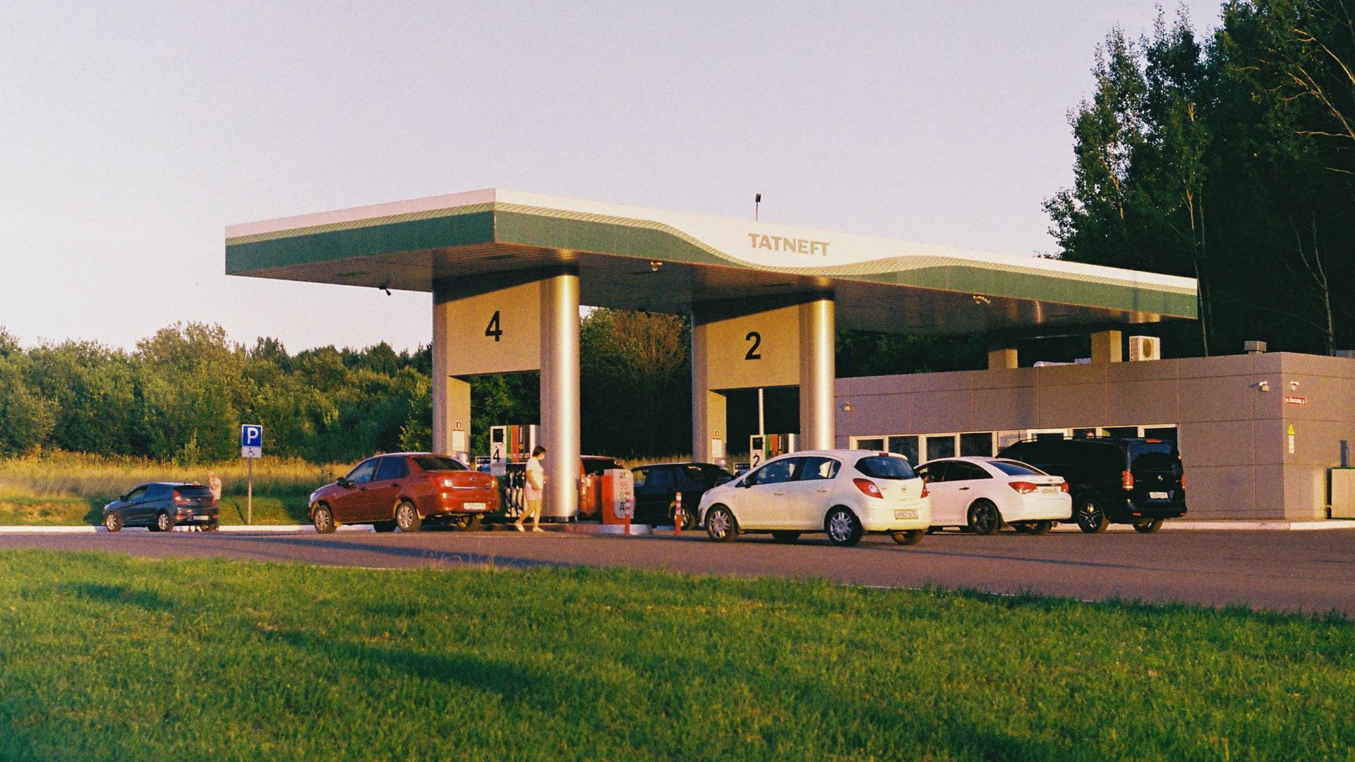 Cars lined up at a Tatneft gas station with a green landscape backdrop during the day.