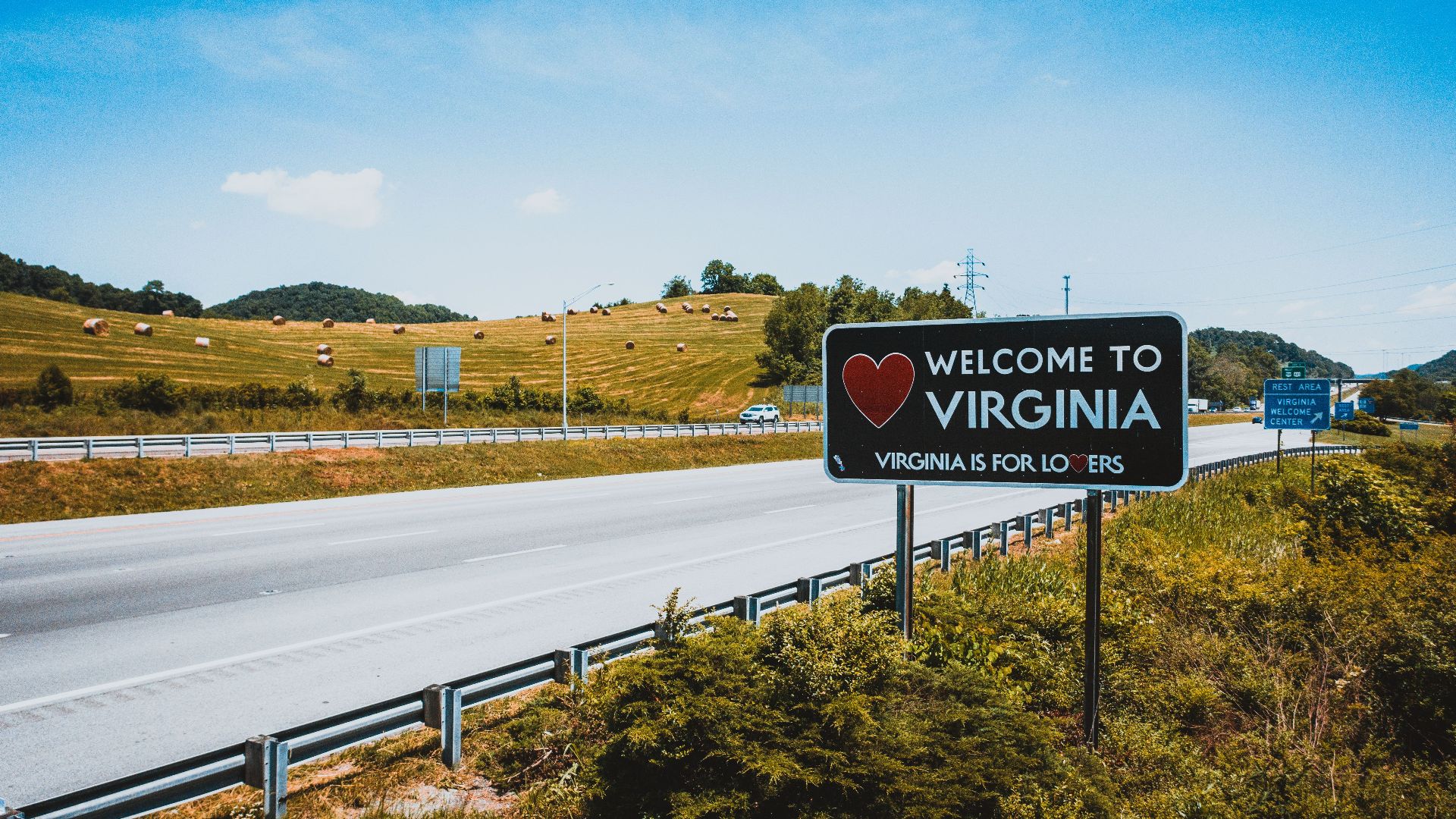 Empty asphalt highway in hilly countryside near road sign with welcome to Virginia inscription on sunny day