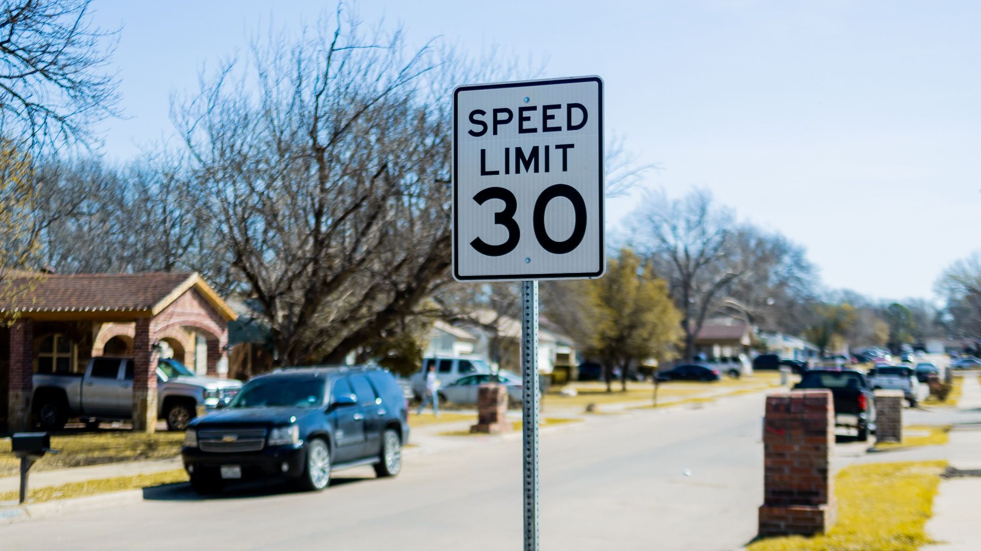 Speed limit 30 sign on a suburban street with cars and houses.