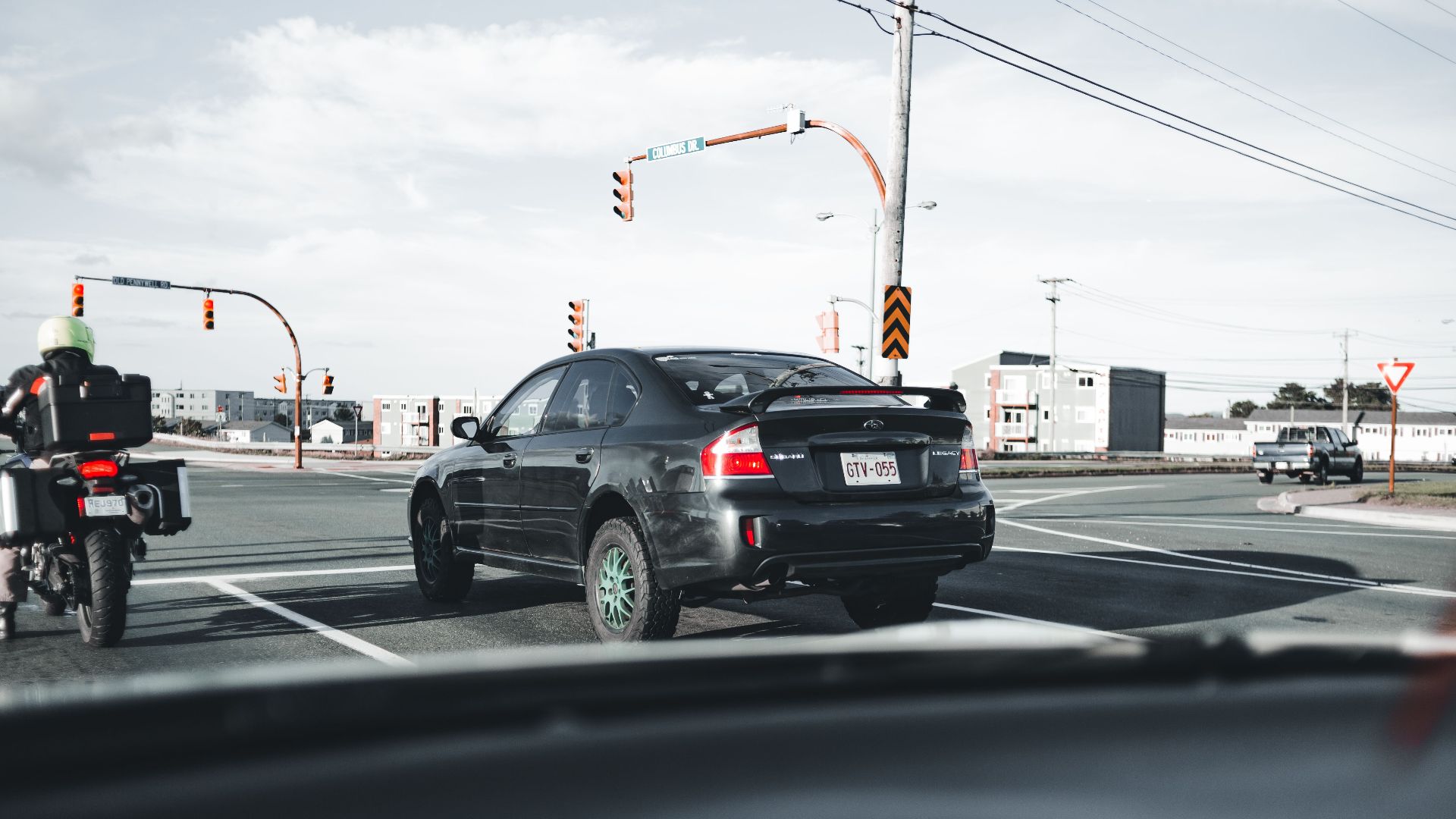 A motorcycle and car wait at a busy city intersection under traffic lights.