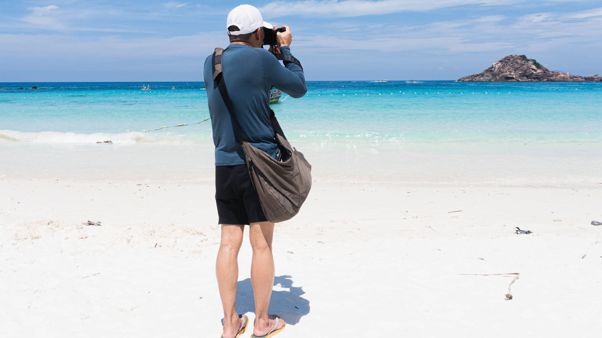 Man taking photos on a beautiful tropical beach with turquoise waters under a clear blue sky.