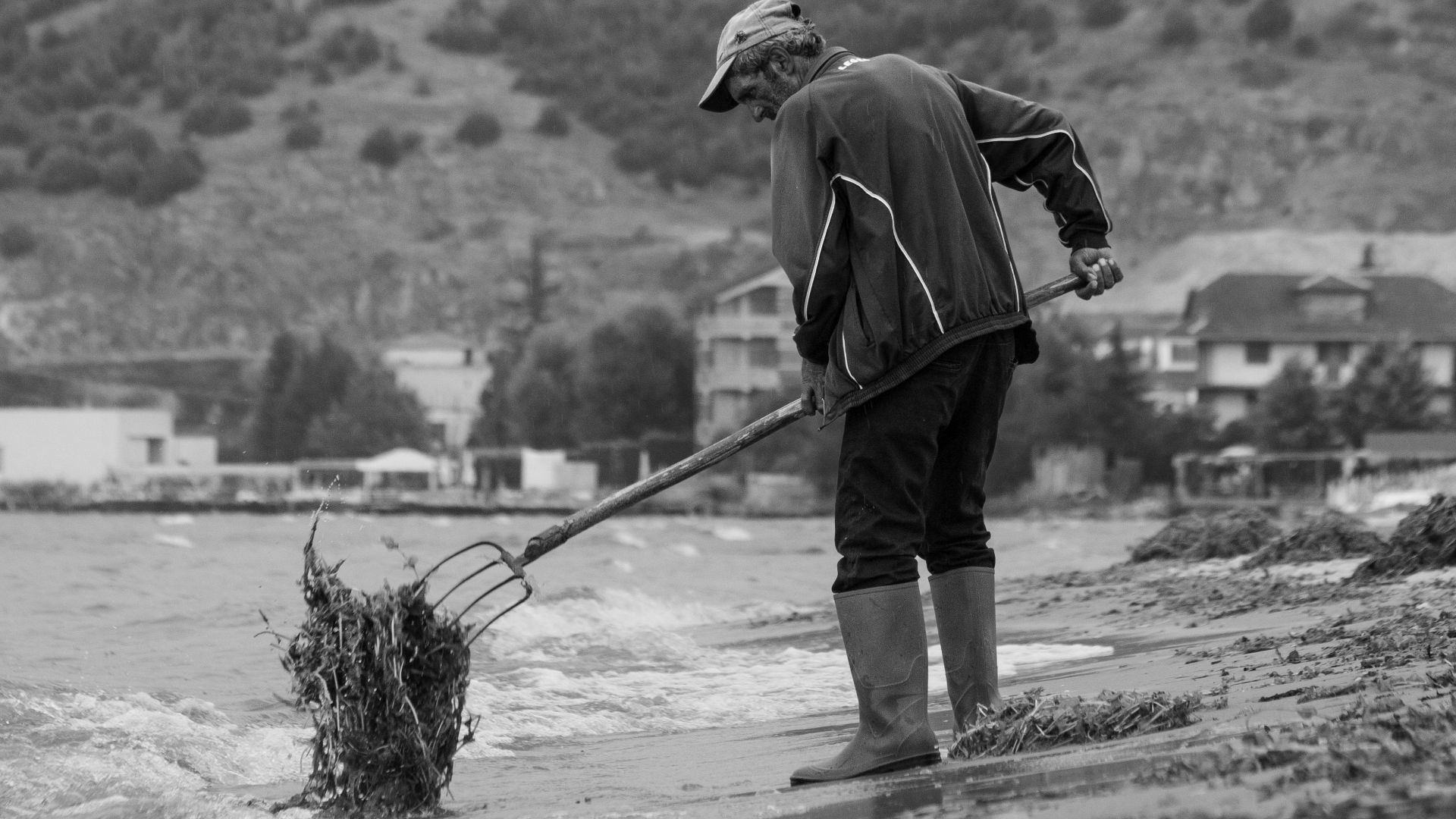 A man cleans the shore at Pogradec, Albania in a dramatic black and white scene.