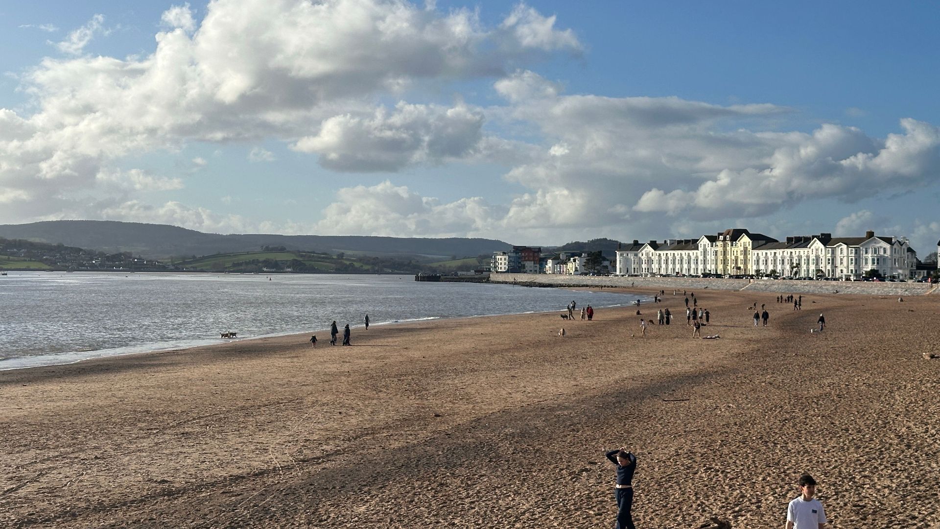 Serene beach scene with people and coastal town under blue sky.