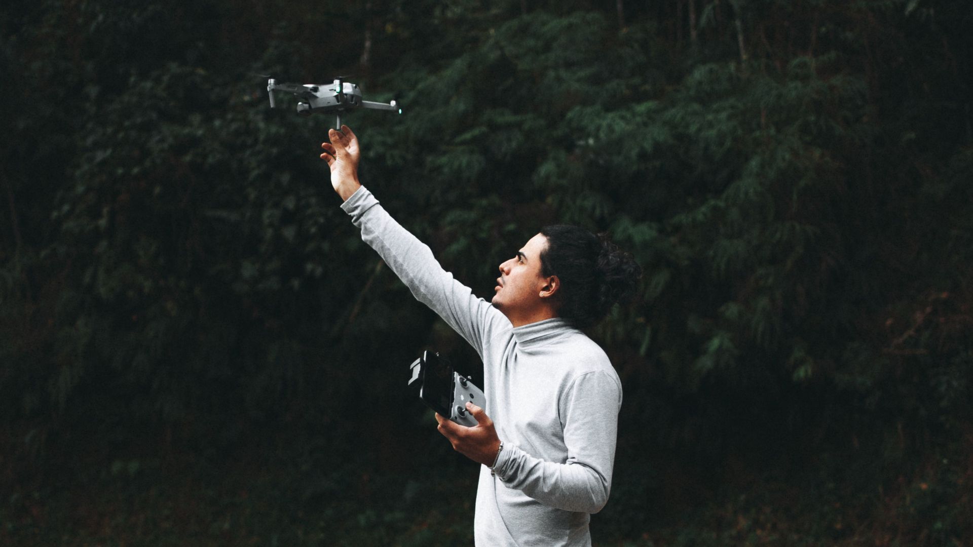 A man operates a drone on a quiet forest road, capturing nature's tranquility.