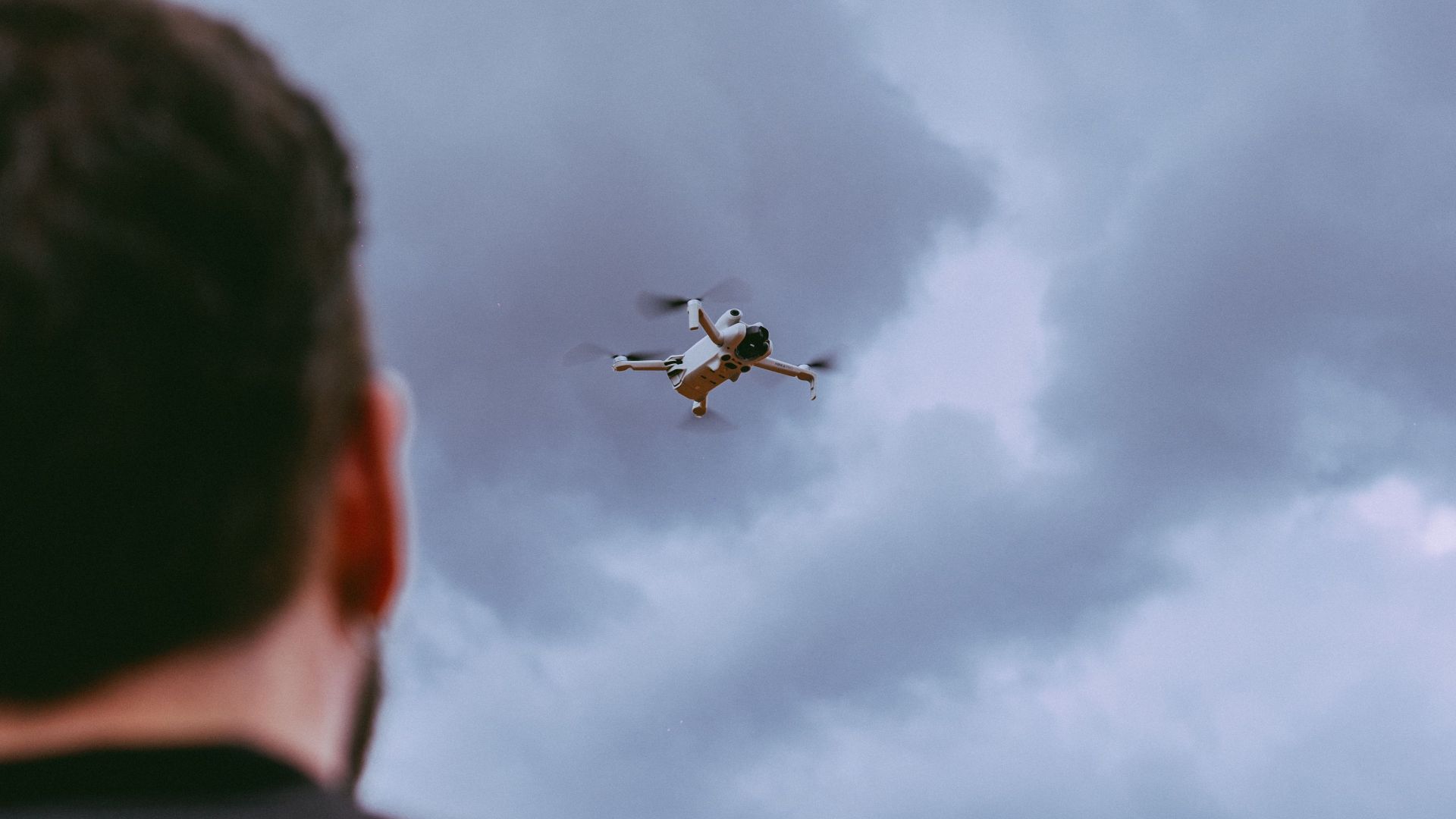 Person observing a drone against a dramatic cloudy backdrop, showcasing aerial technology.