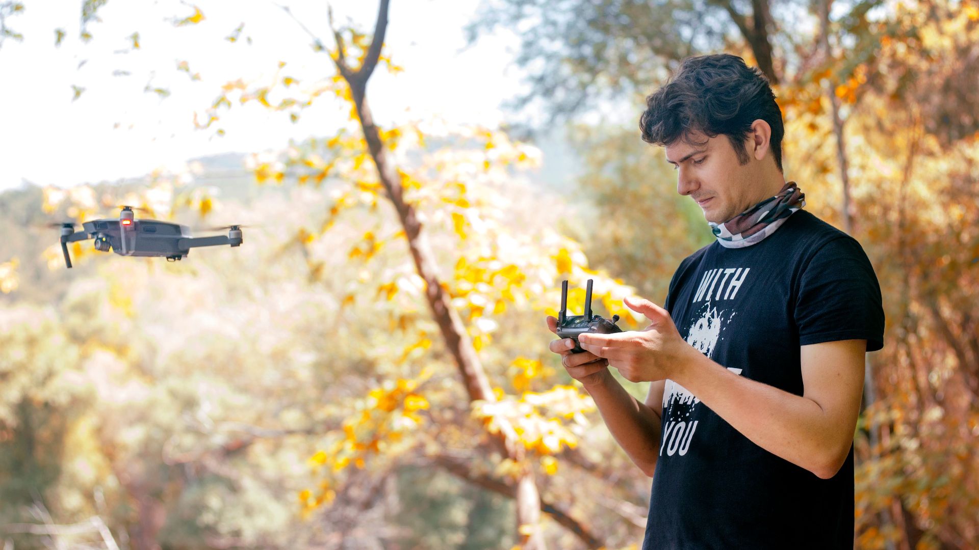 A young man controls a drone in a vibrant autumn park, capturing scenic views.