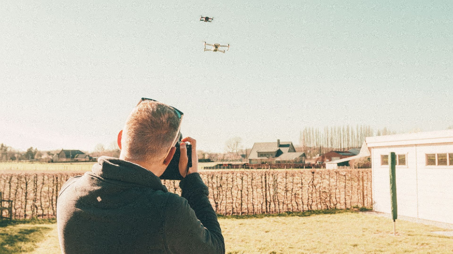 A man controls a flying drone in a bright and sunny open field setting.