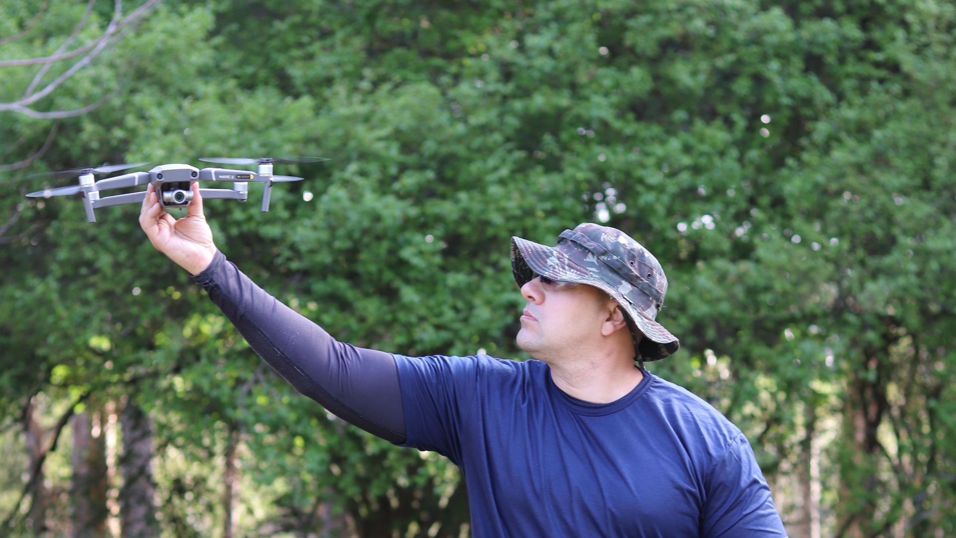 A man in tactical gear controls a flying drone outdoors, showcasing modern technology in action.