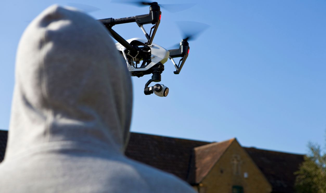 Hooded man looking up at a surveillance drone in the blue sky