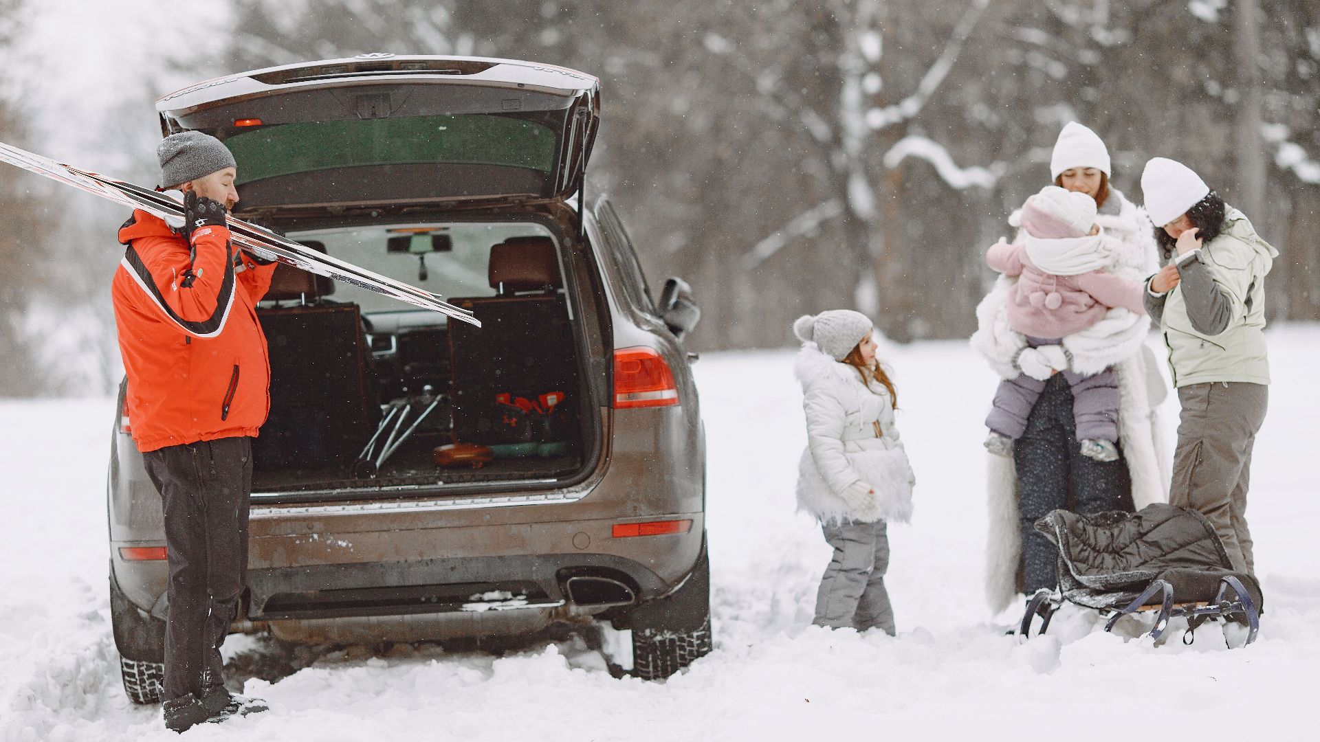 A family gears up for winter fun, unpacking skis and sleds from a car in a snowy landscape.
