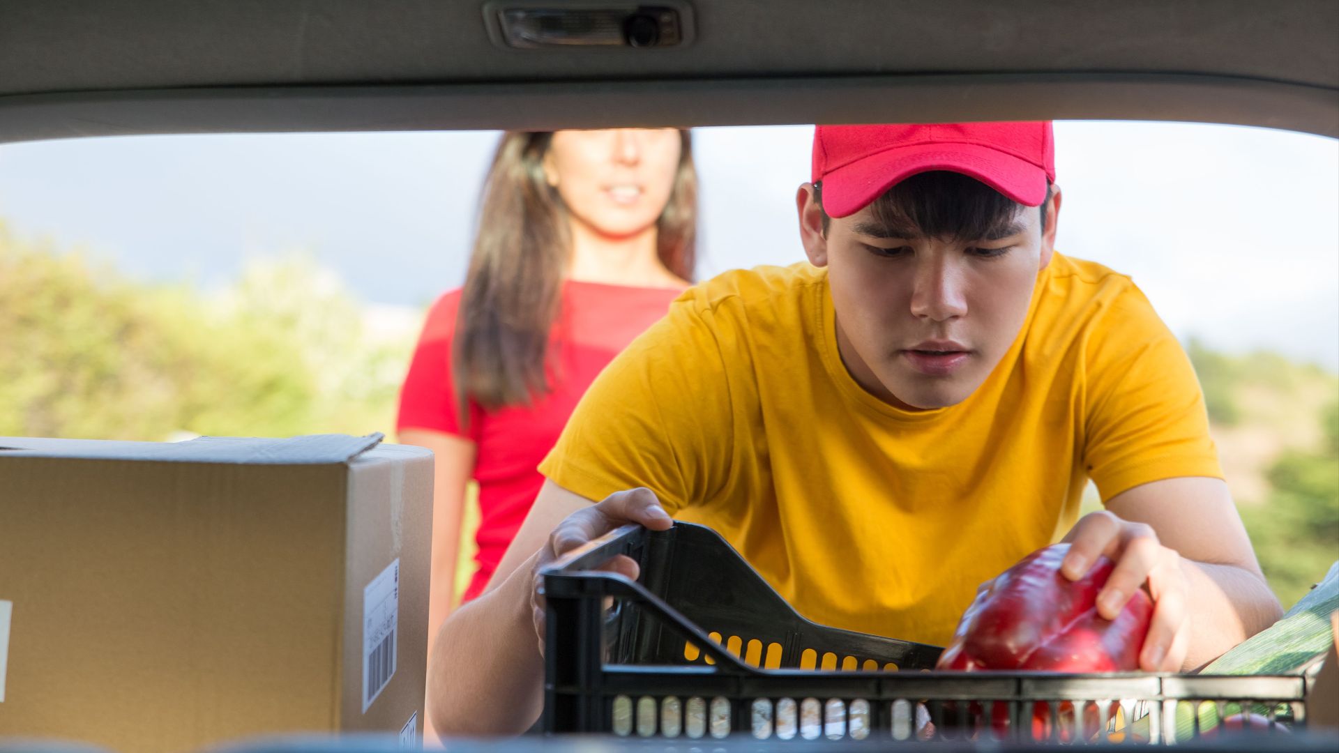Man in yellow shirt loading groceries into a vehicle, outdoors.