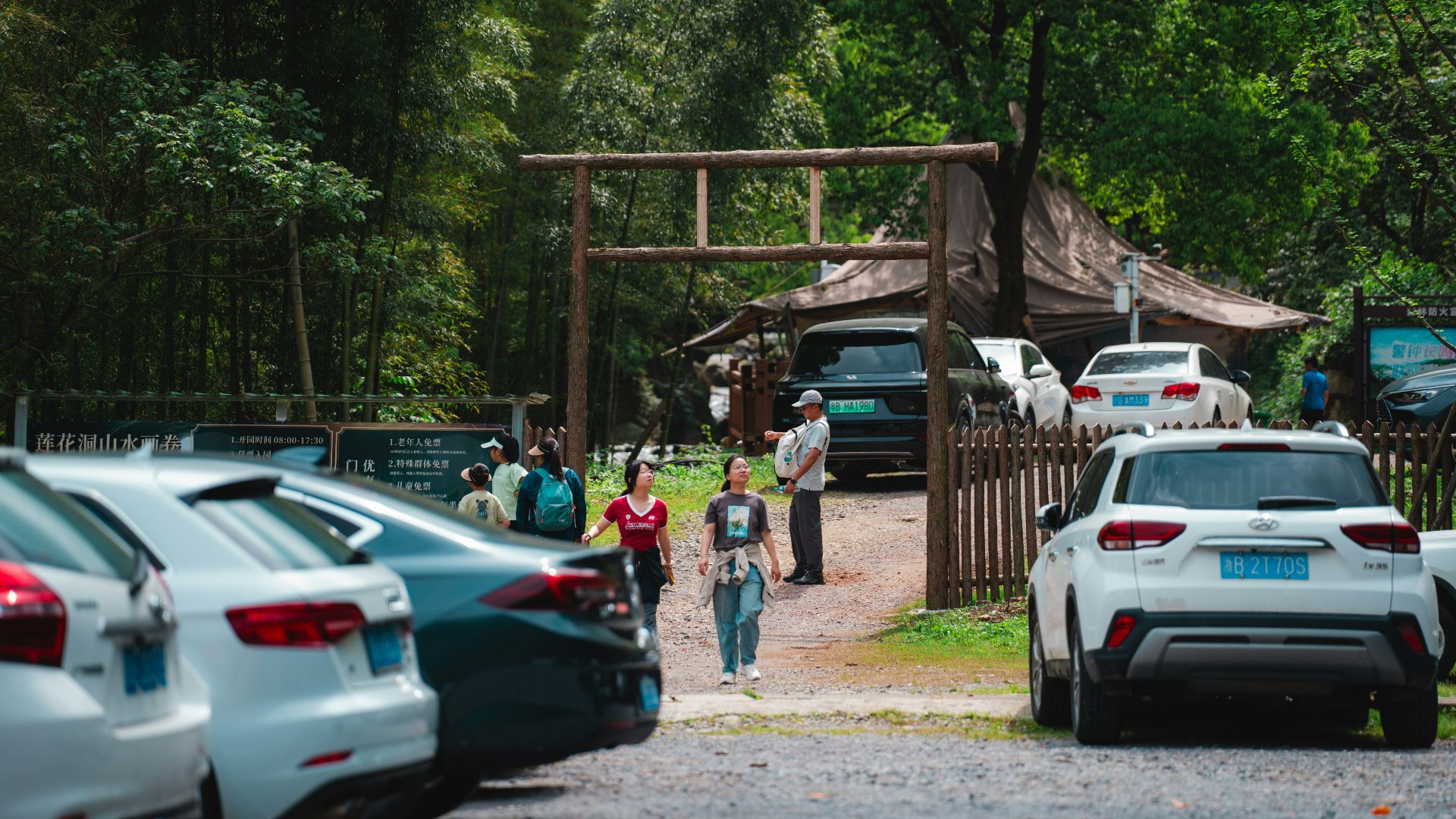 Cars parked near a wooden gate with people walking.