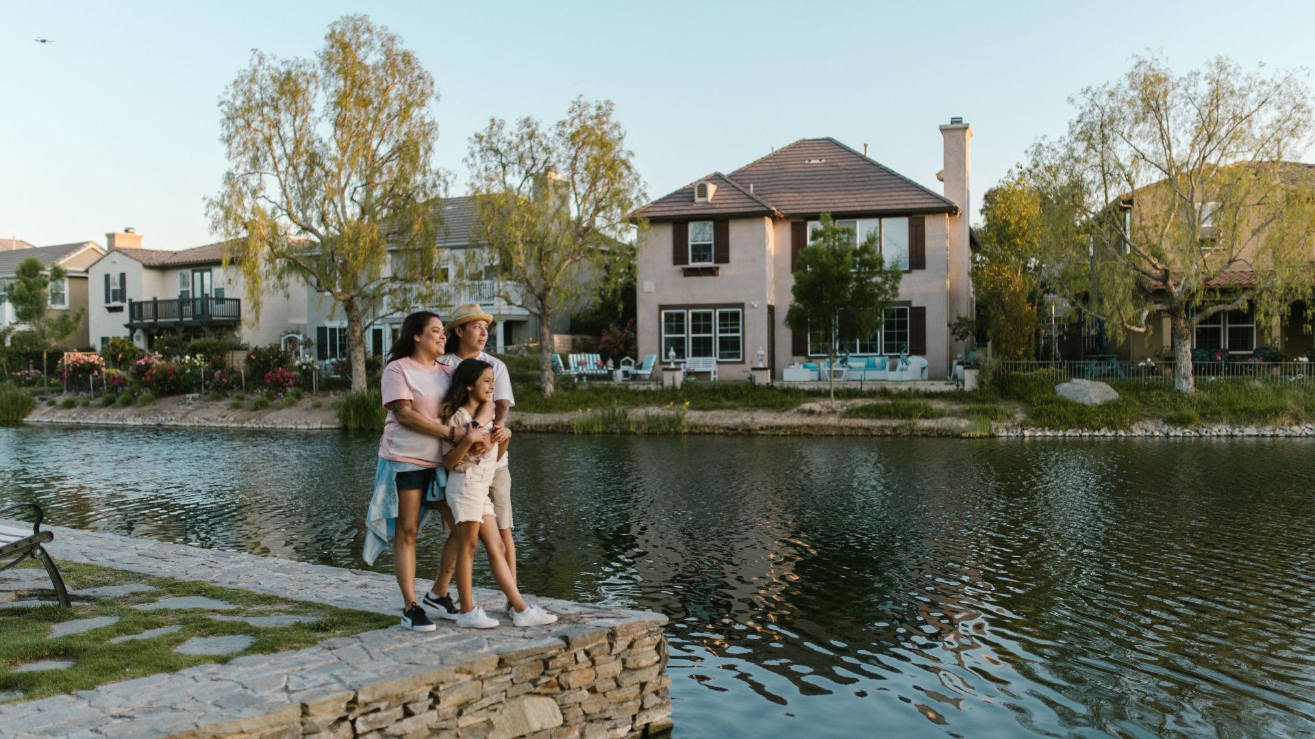 A family embraces by a lakeside in a picturesque urban neighborhood, capturing a moment of love and togetherness.