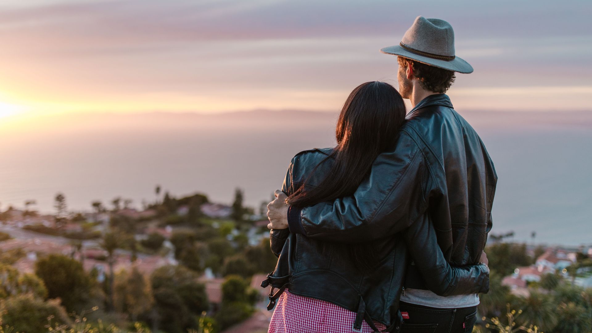 Romantic couple embraces while watching the sun set over the ocean, creating a tranquil moment.