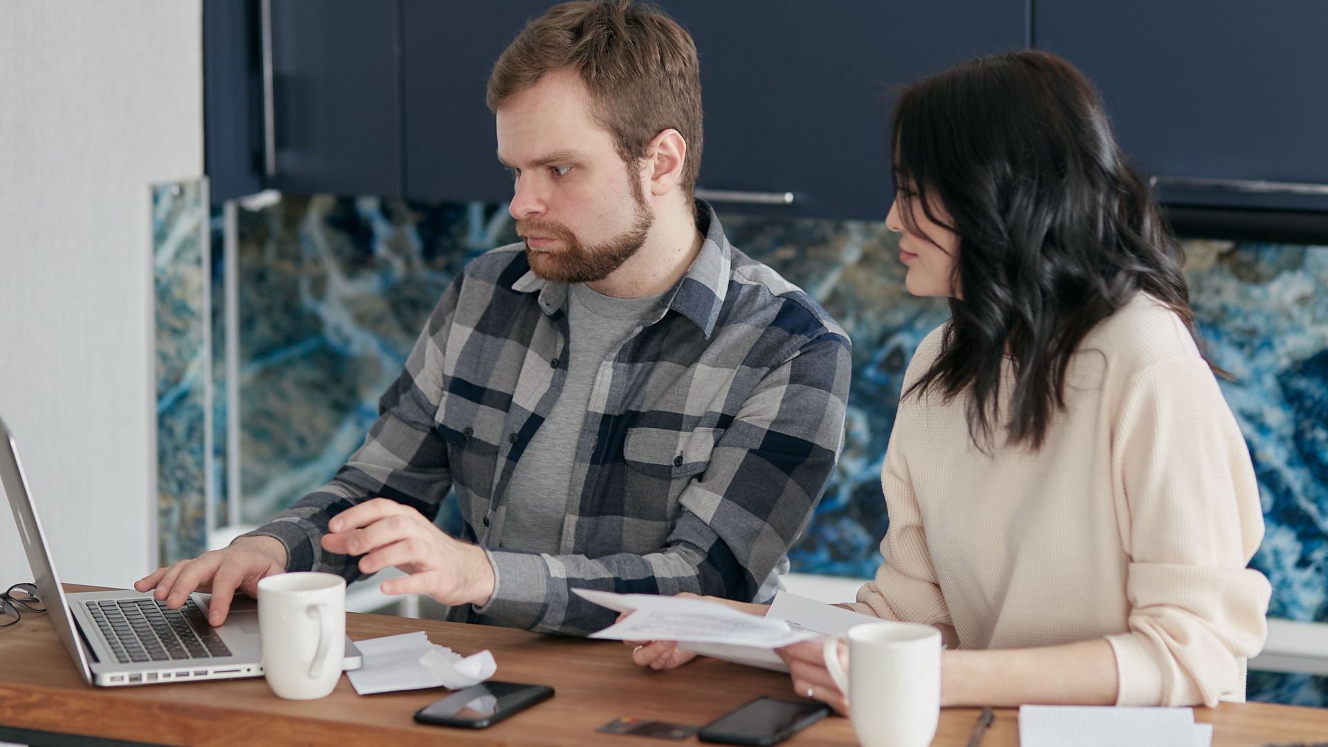 A couple working together on a laptop managing finances at home, showcasing teamwork and concentration.