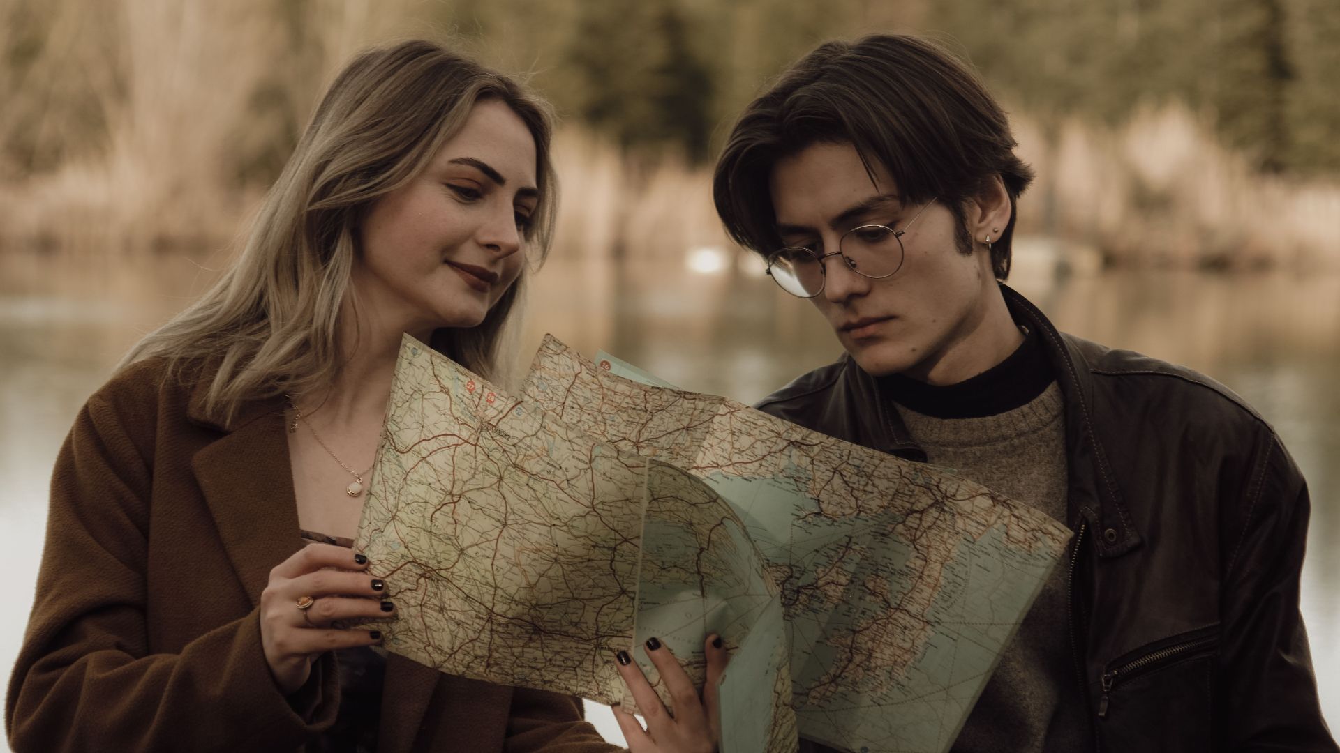 Young couple analyzing a map by a serene lake, planning their travel route in a tranquil nature setting.