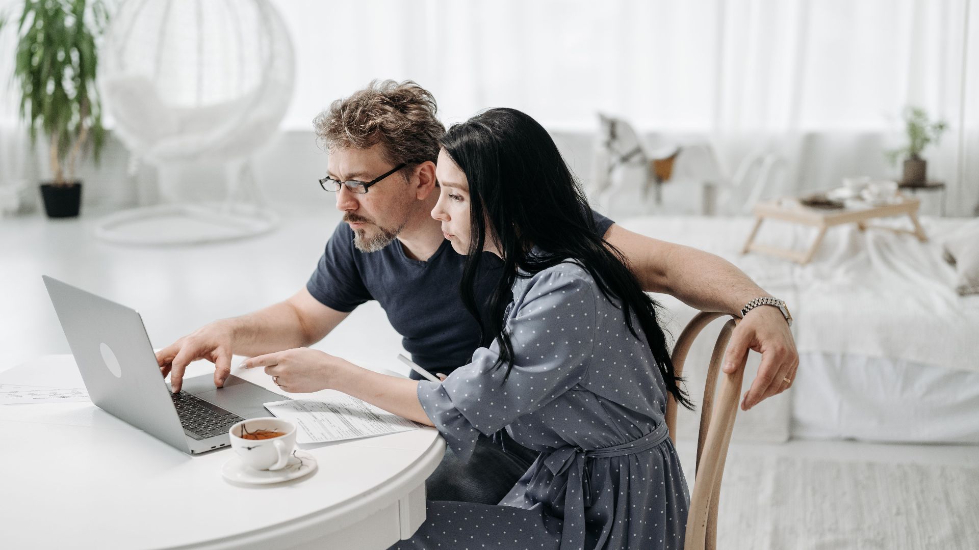 A man and woman sitting indoors, collaborating on a laptop at a table with coffee.