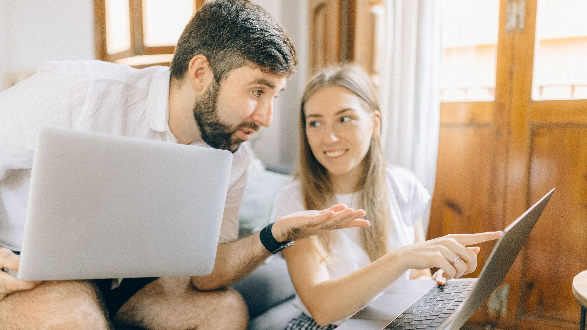 Young couple sitting together, discussing something on their laptops in a cozy room.