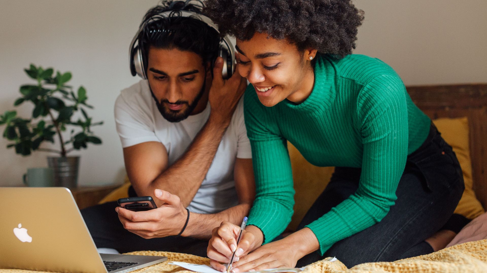 A smiling couple working together at home with laptop and headphones.