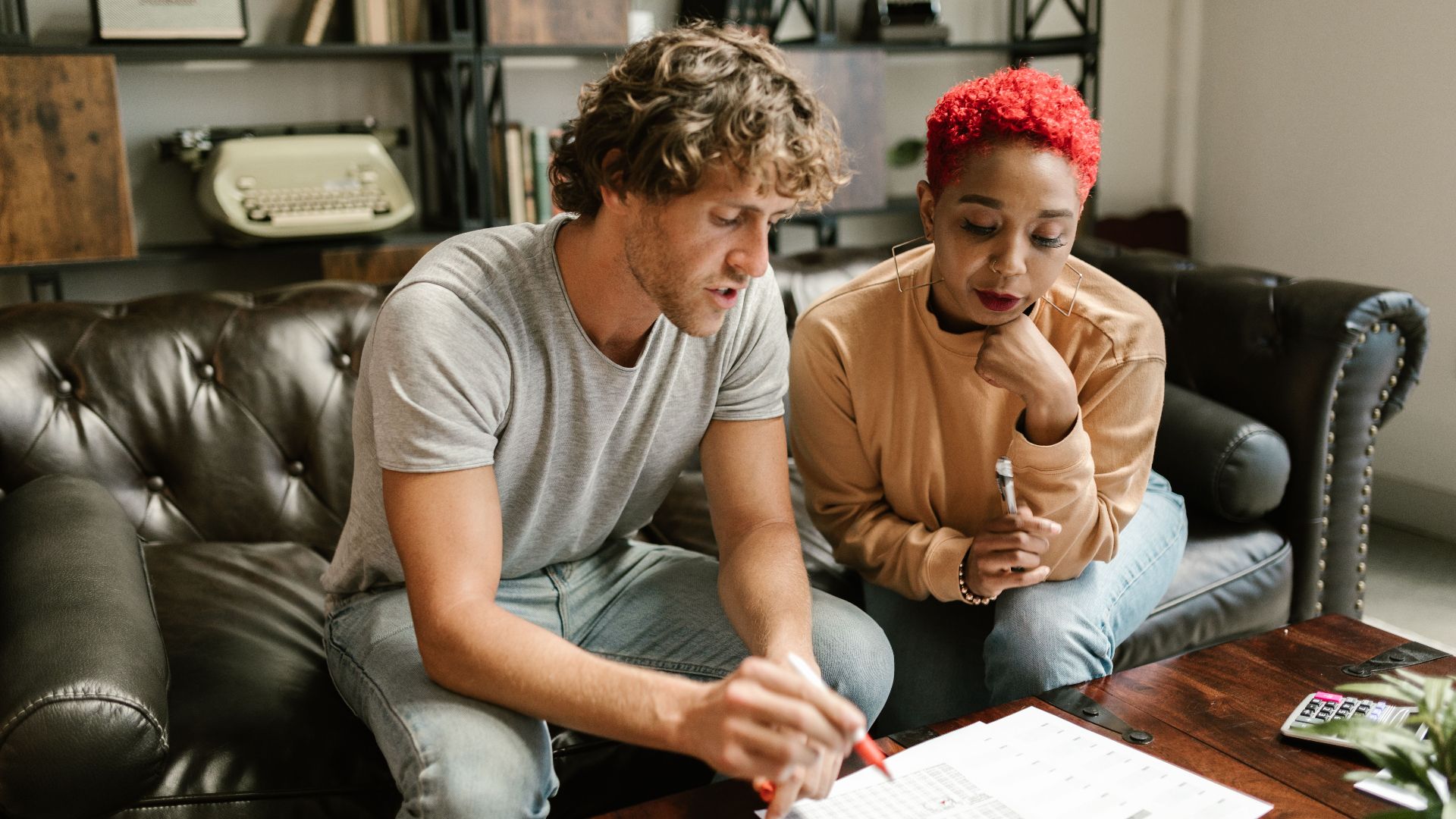 A couple sitting on a sofa examines documents in a cozy, modern living room setting.