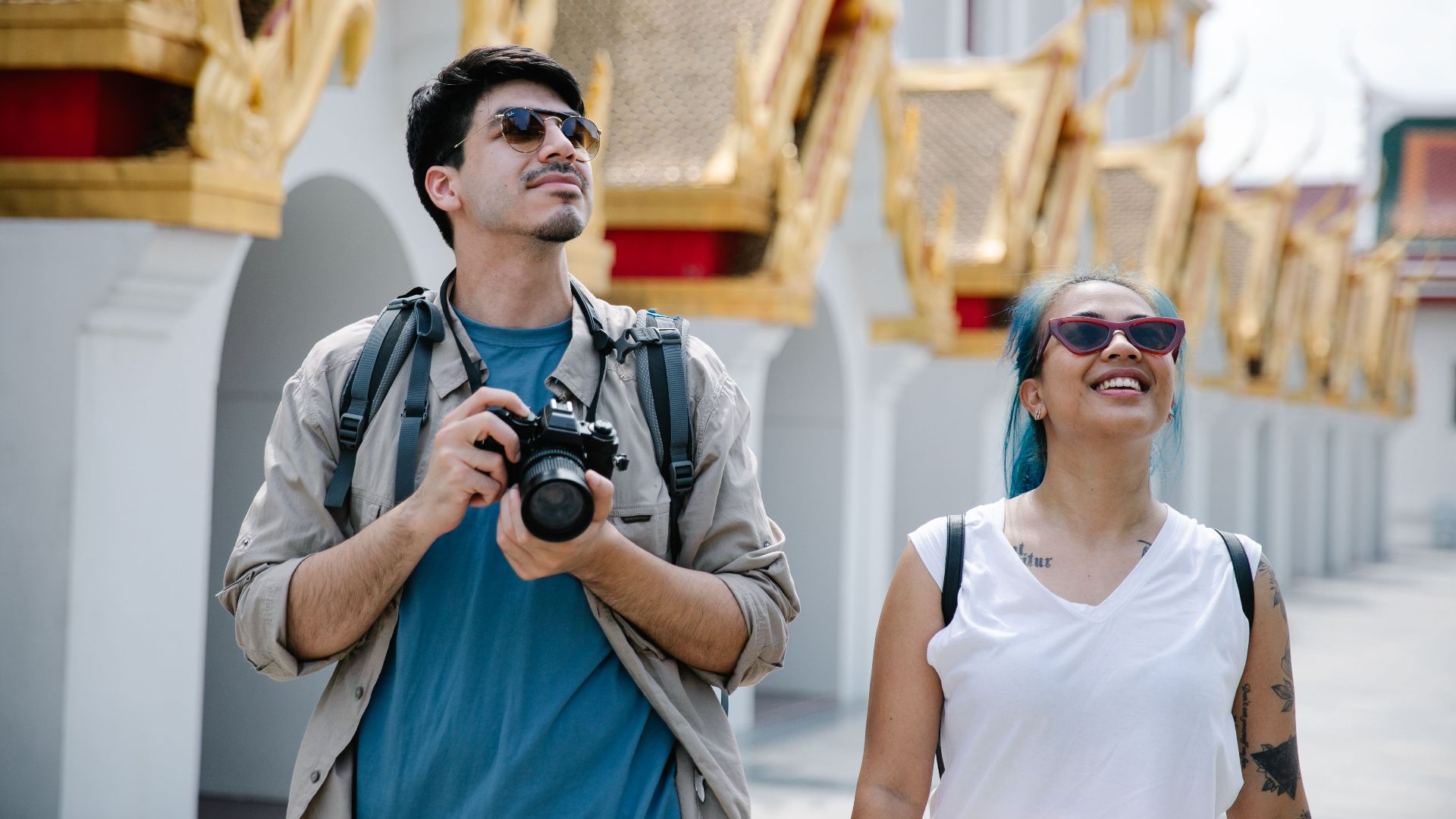 A couple explores a city's ornate architecture, capturing memories with a camera.