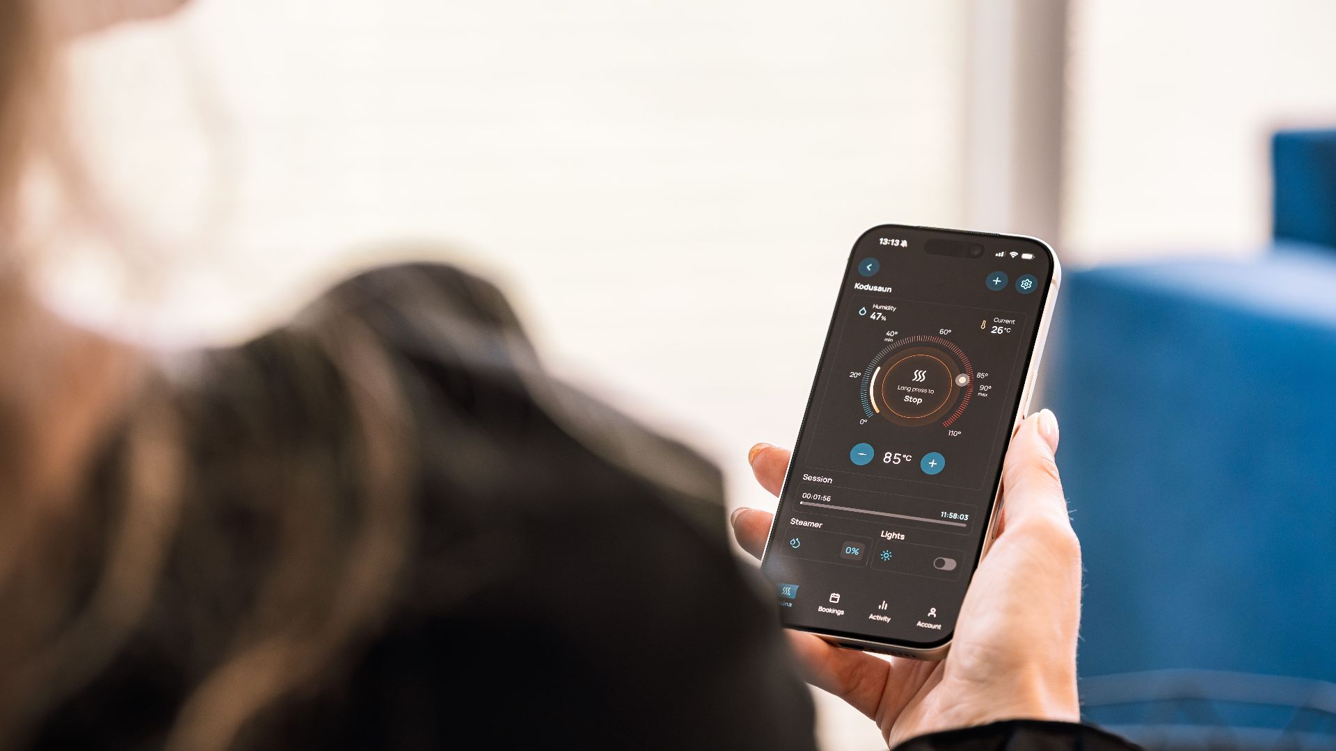 A woman holding a smartphone displaying a sauna control app, highlighting modern sauna technology.