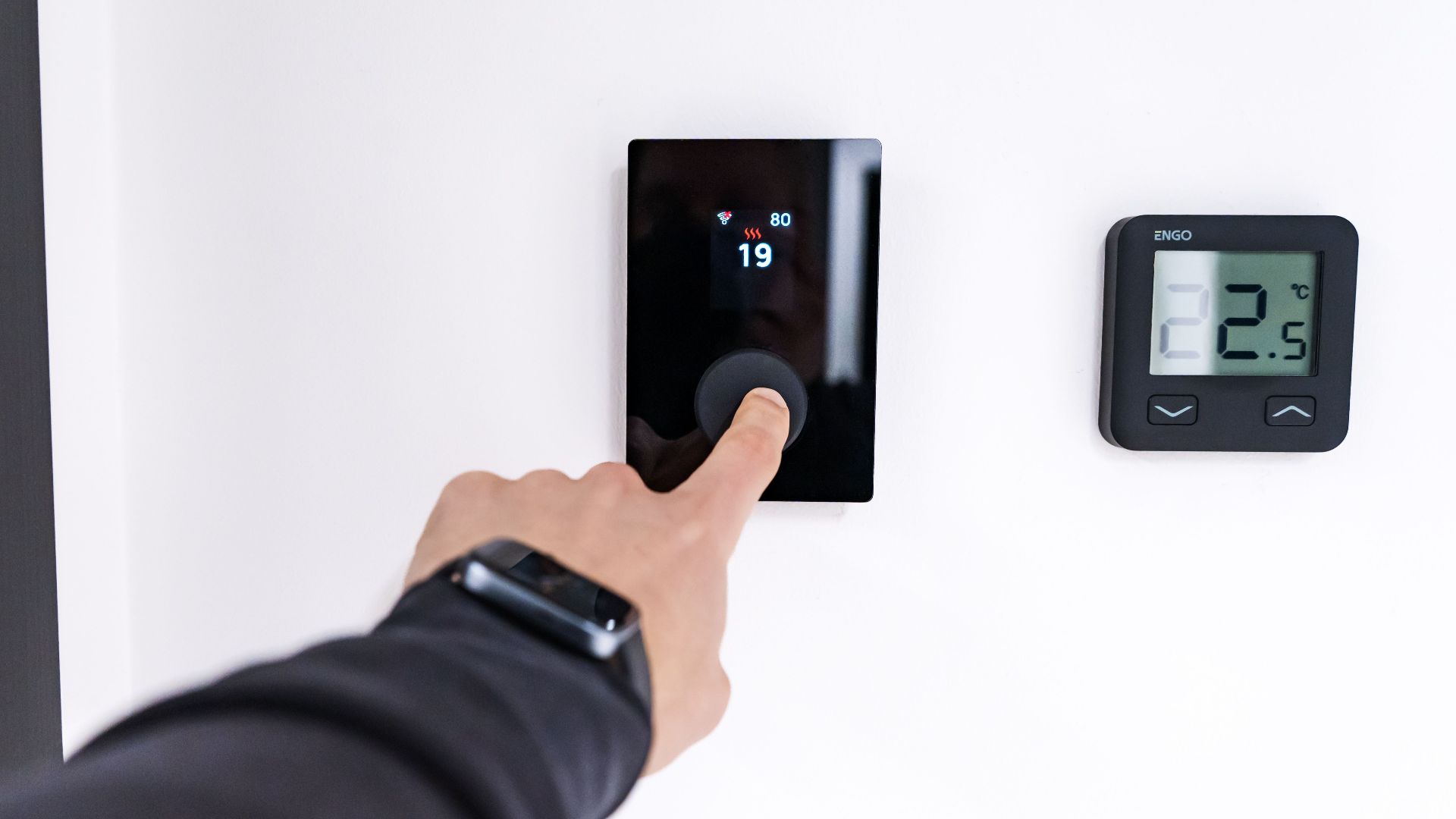 A hand adjusting a digital thermostat in a modern home interior, showcasing smart home technology.