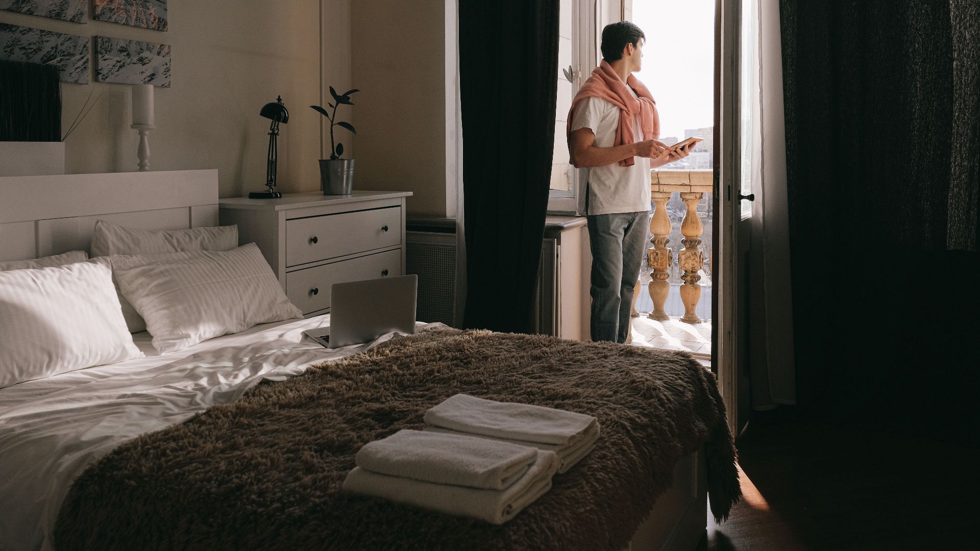 A man stands on a bedroom balcony using a tablet, capturing a moment of relaxation and contemplation.