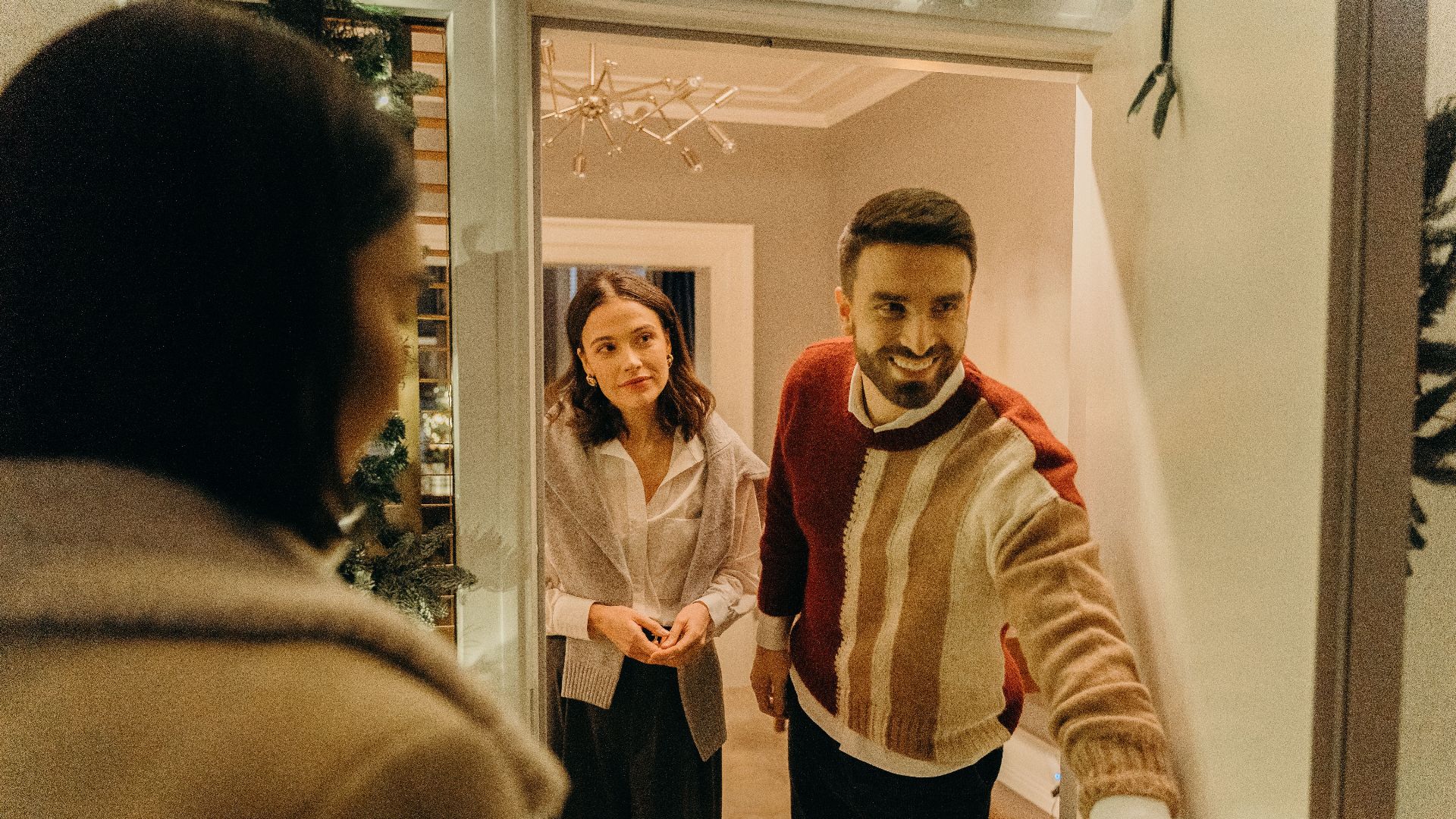 A couple greeting a guest at their doorway, capturing the warmth of a home during the holiday season.