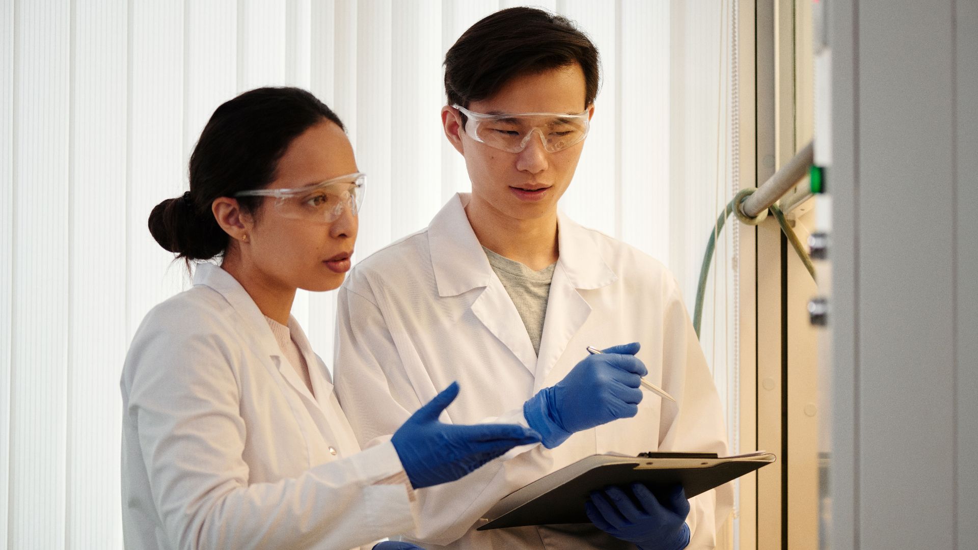 Researchers discussing data in a laboratory setting, wearing safety gear and blue gloves.