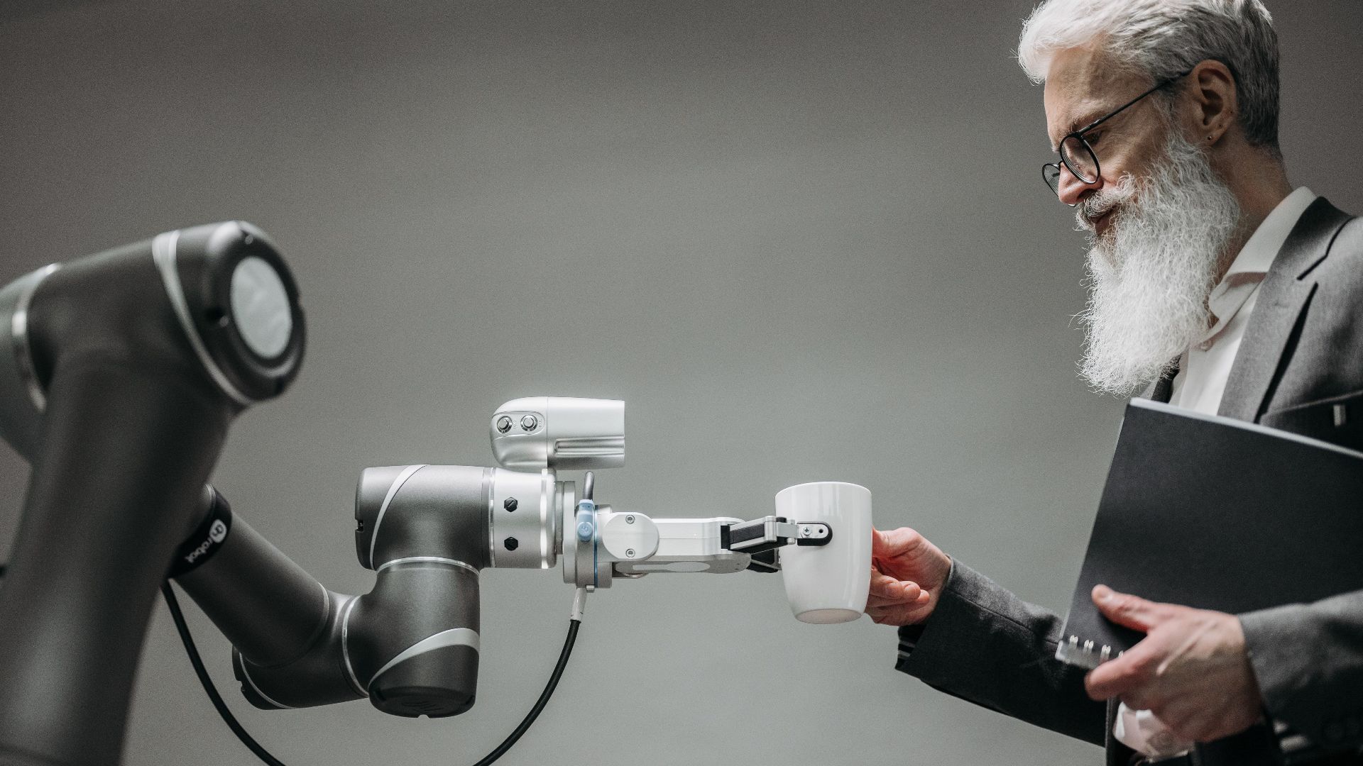 An elderly man receives a cup from a robotic arm in a modern office setting.