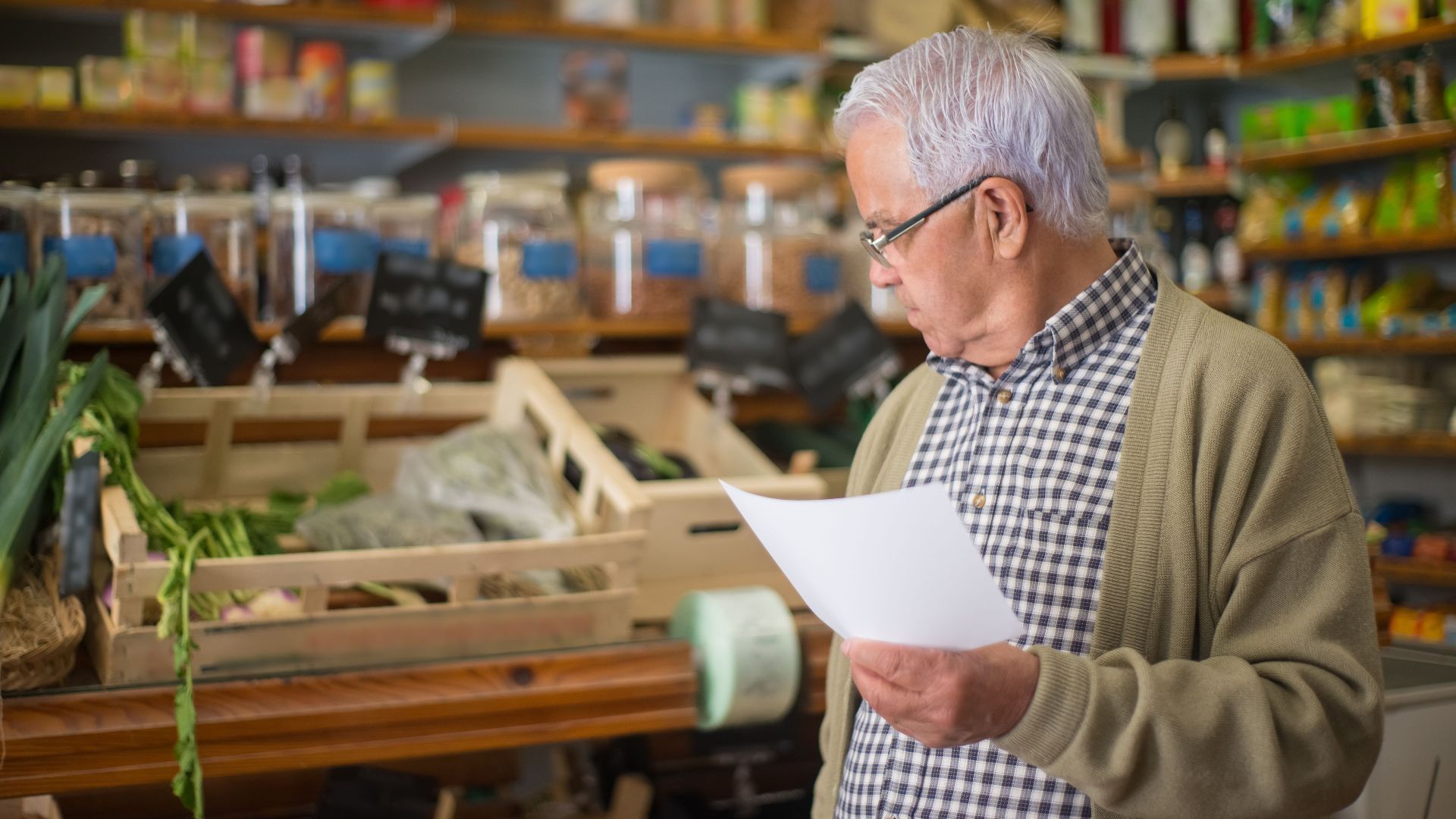 Senior man shopping in a Portuguese store, holding a shopping list.