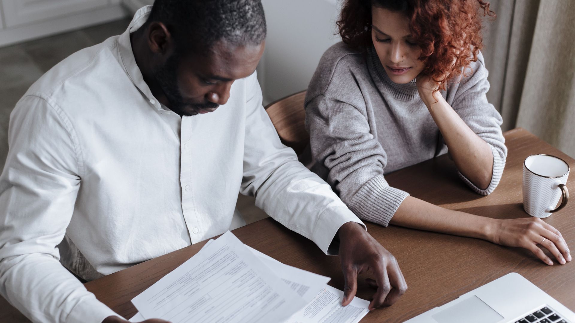 A couple reviews important documents together at a home desk with a laptop.